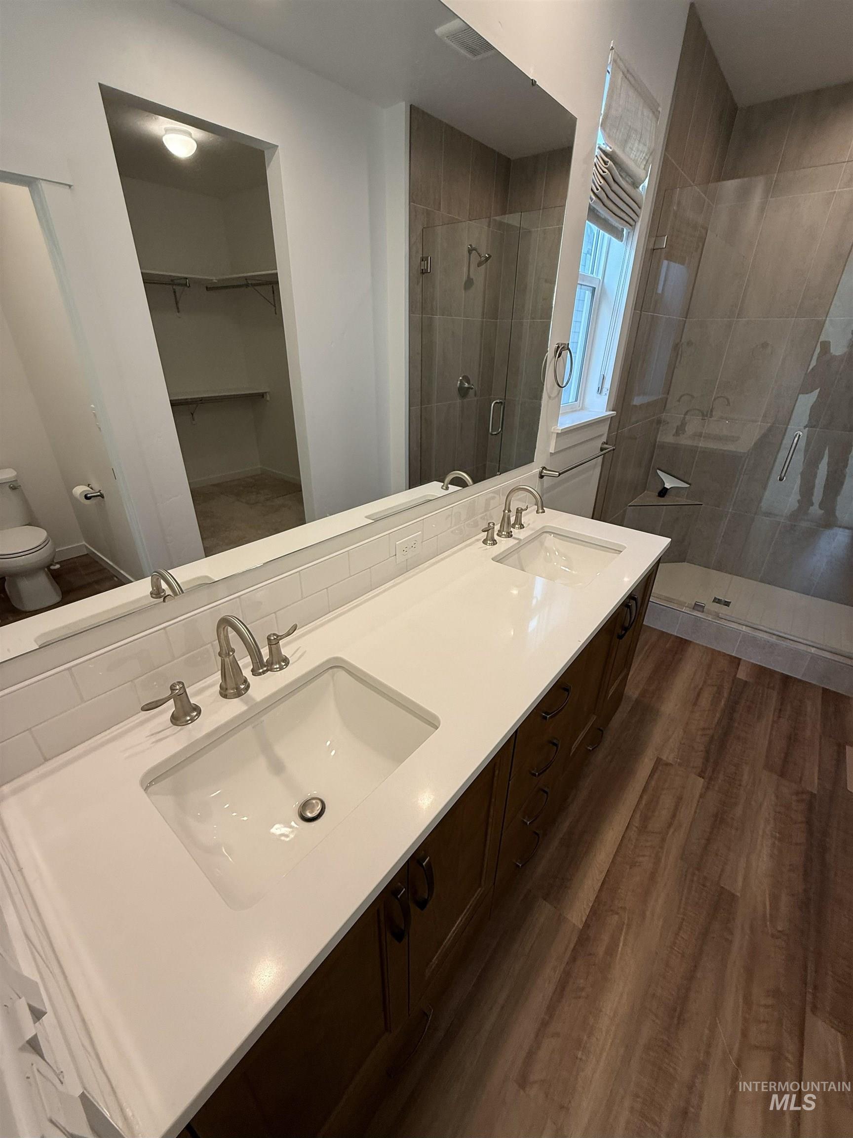 Bathroom featuring a shower stall, double vanity, a walk in closet, and dark wood finished floors
