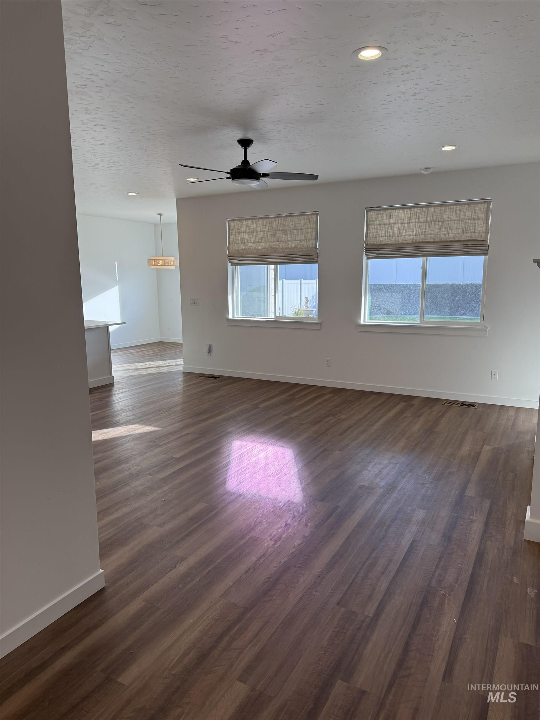 Unfurnished living room with a textured ceiling, dark wood-type flooring, plenty of natural light, recessed lighting, and ceiling fan