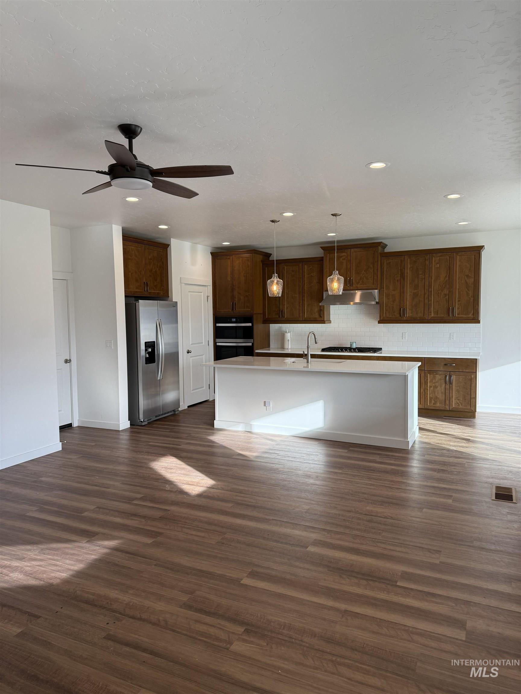 Kitchen with pendant lighting, dark wood-type flooring, stainless steel refrigerator with ice dispenser, open floor plan, and recessed lighting