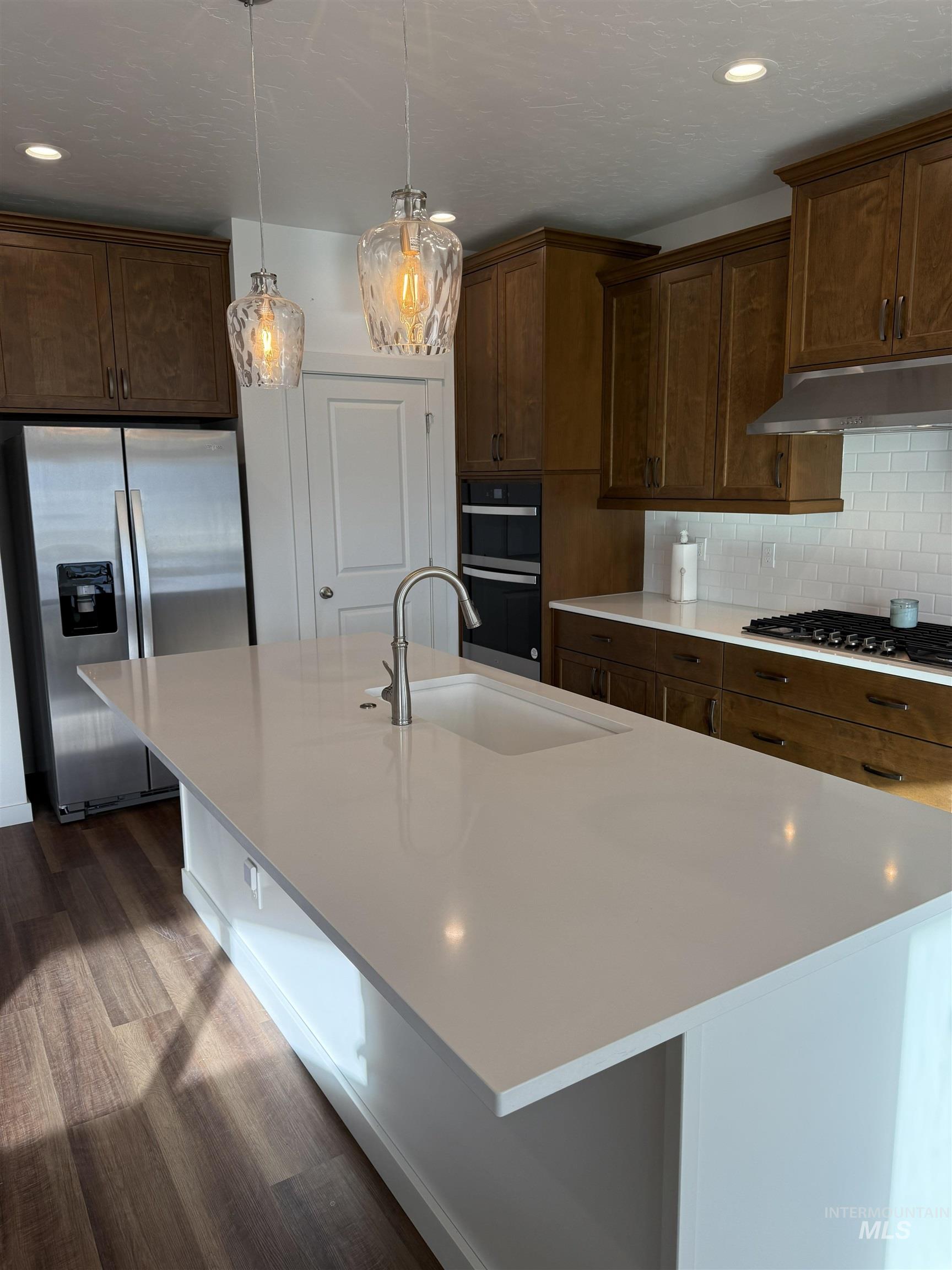 Kitchen featuring stainless steel appliances, an island with sink, pendant lighting, backsplash, and under cabinet range hood