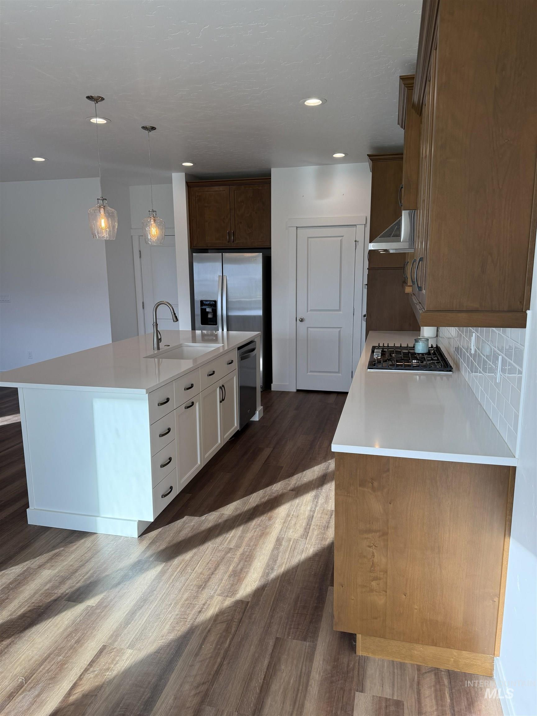 Kitchen with a center island with sink, hanging light fixtures, appliances with stainless steel finishes, dark wood finished floors, and light stone counters