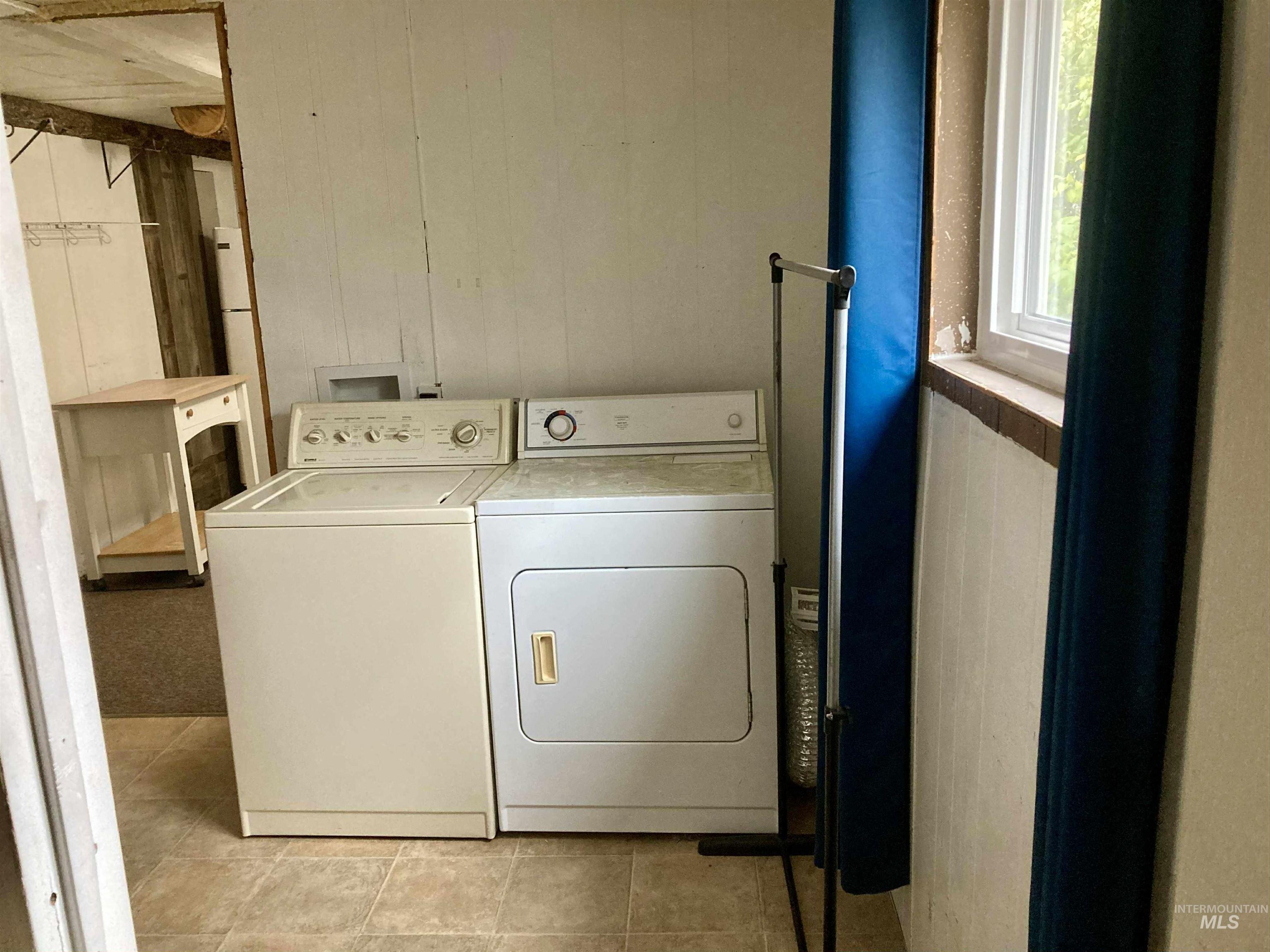 Laundry area featuring wooden walls, light tile patterned floors, and washing machine and dryer