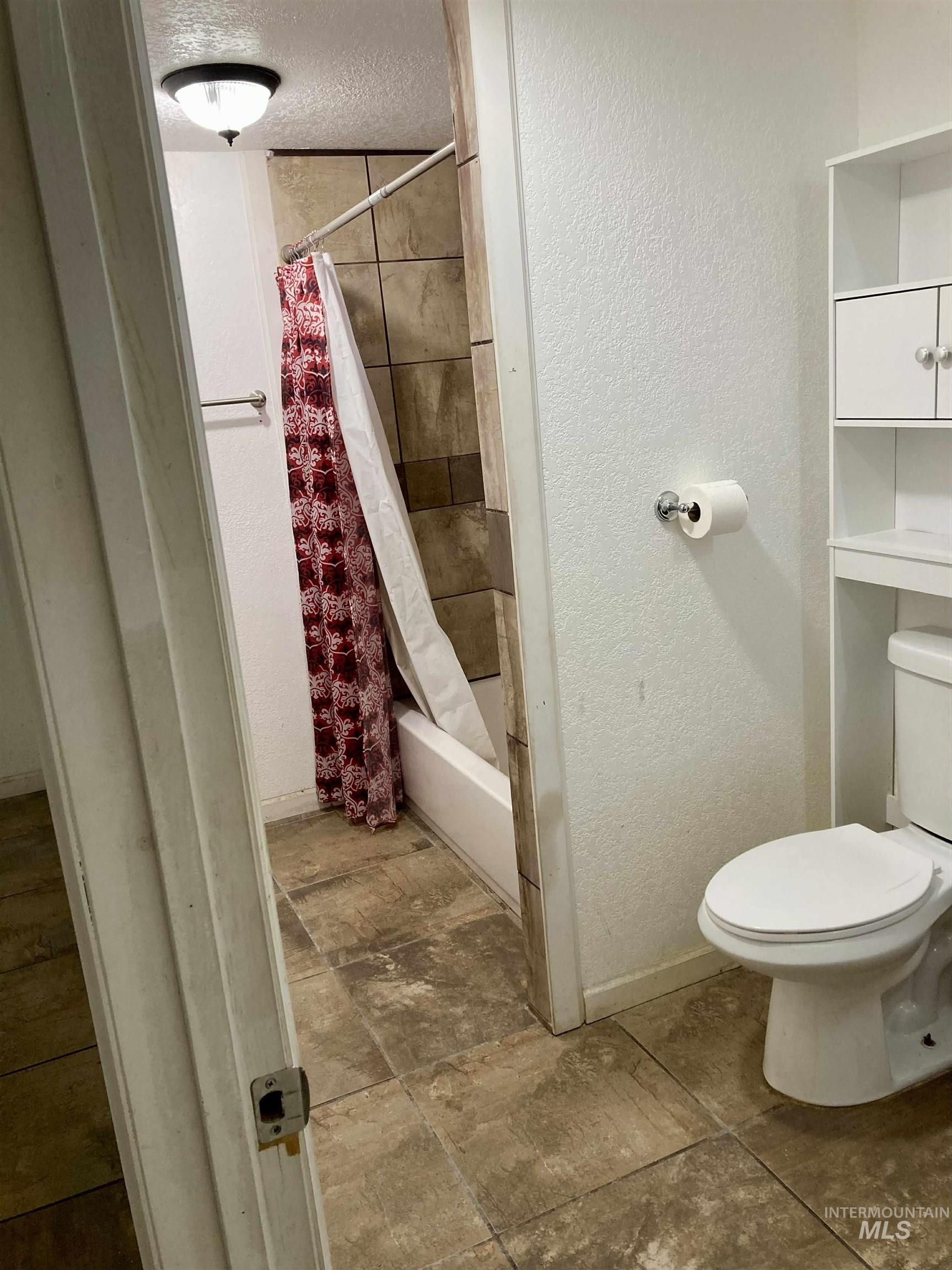 Bathroom with a textured wall, shower / tub combo with curtain, and a textured ceiling