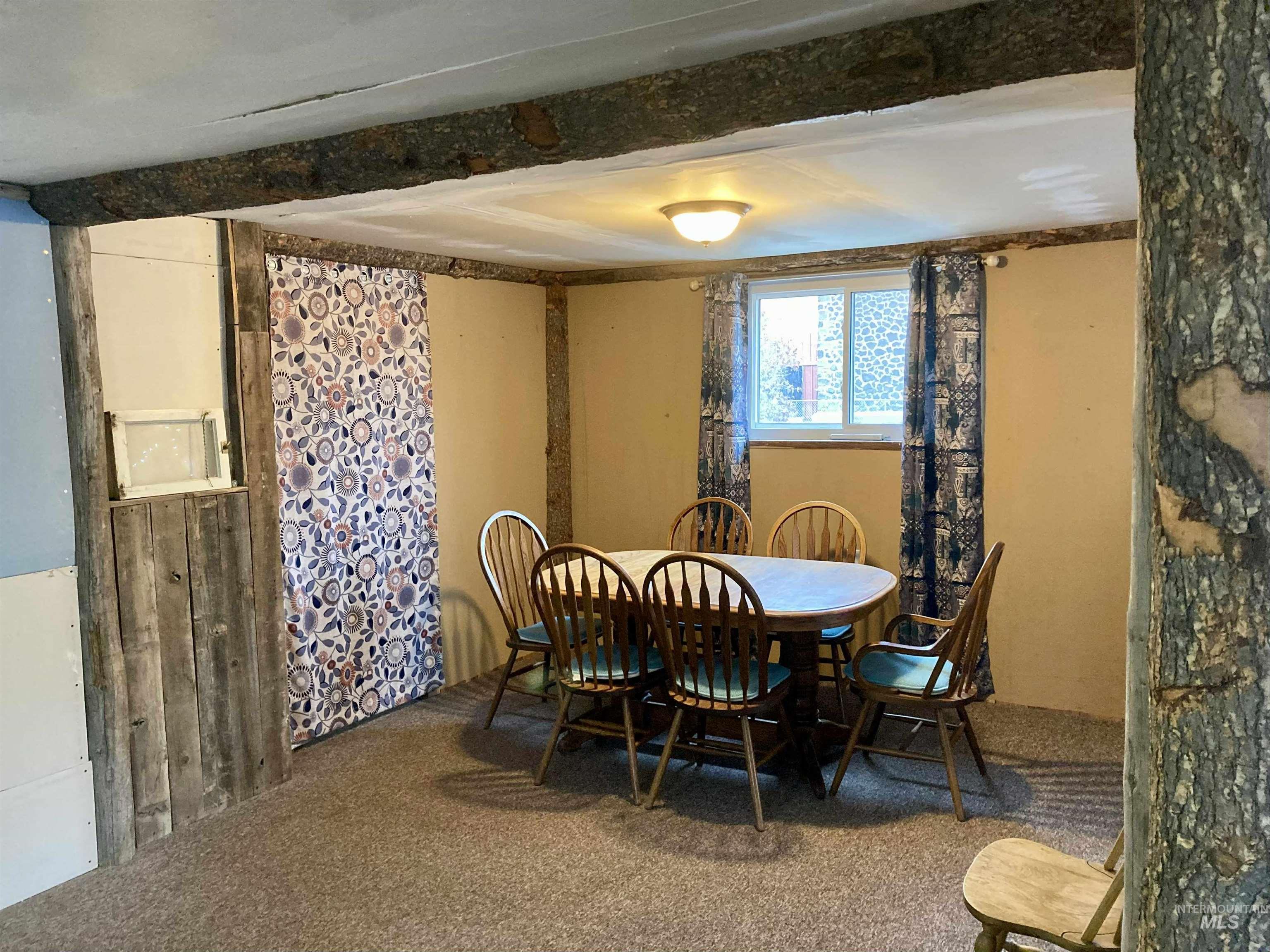 Carpeted dining area featuring beam ceiling