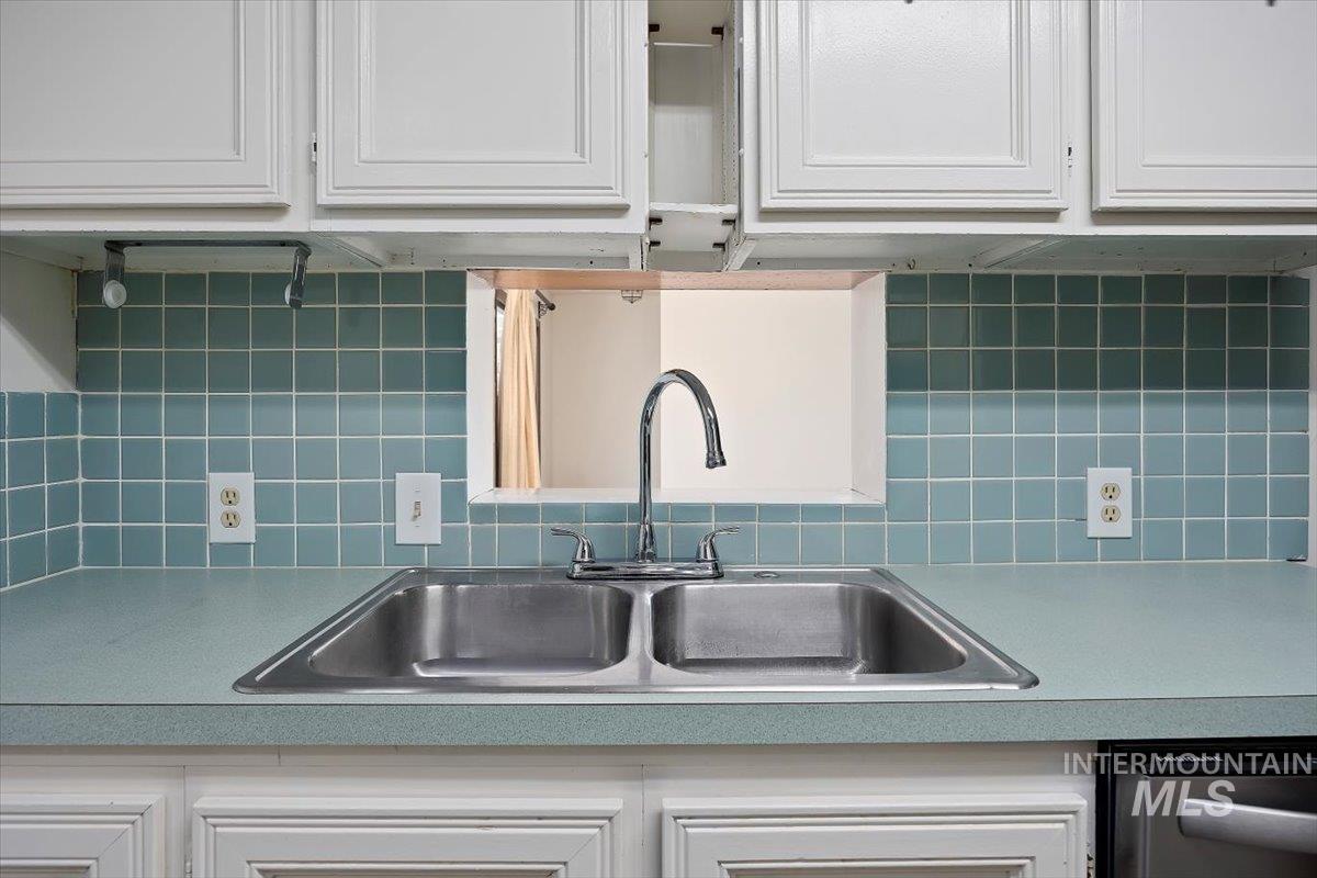 Kitchen with white cabinets, dishwasher, backsplash, and light countertops