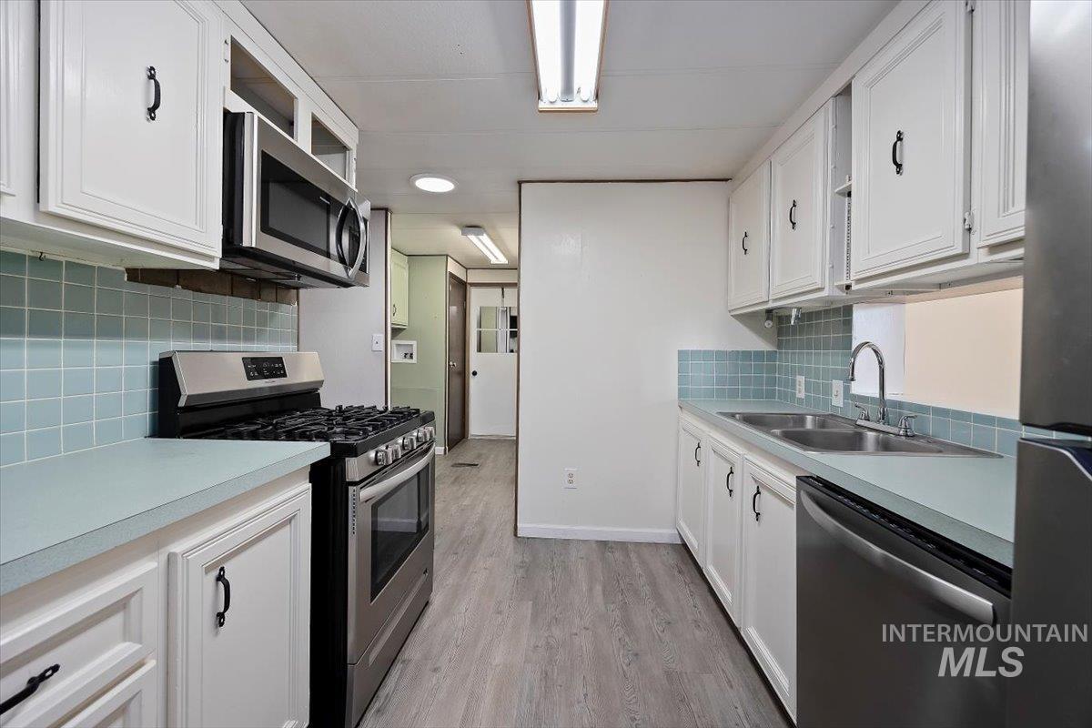 Kitchen with appliances with stainless steel finishes, white cabinetry, and light wood-type flooring