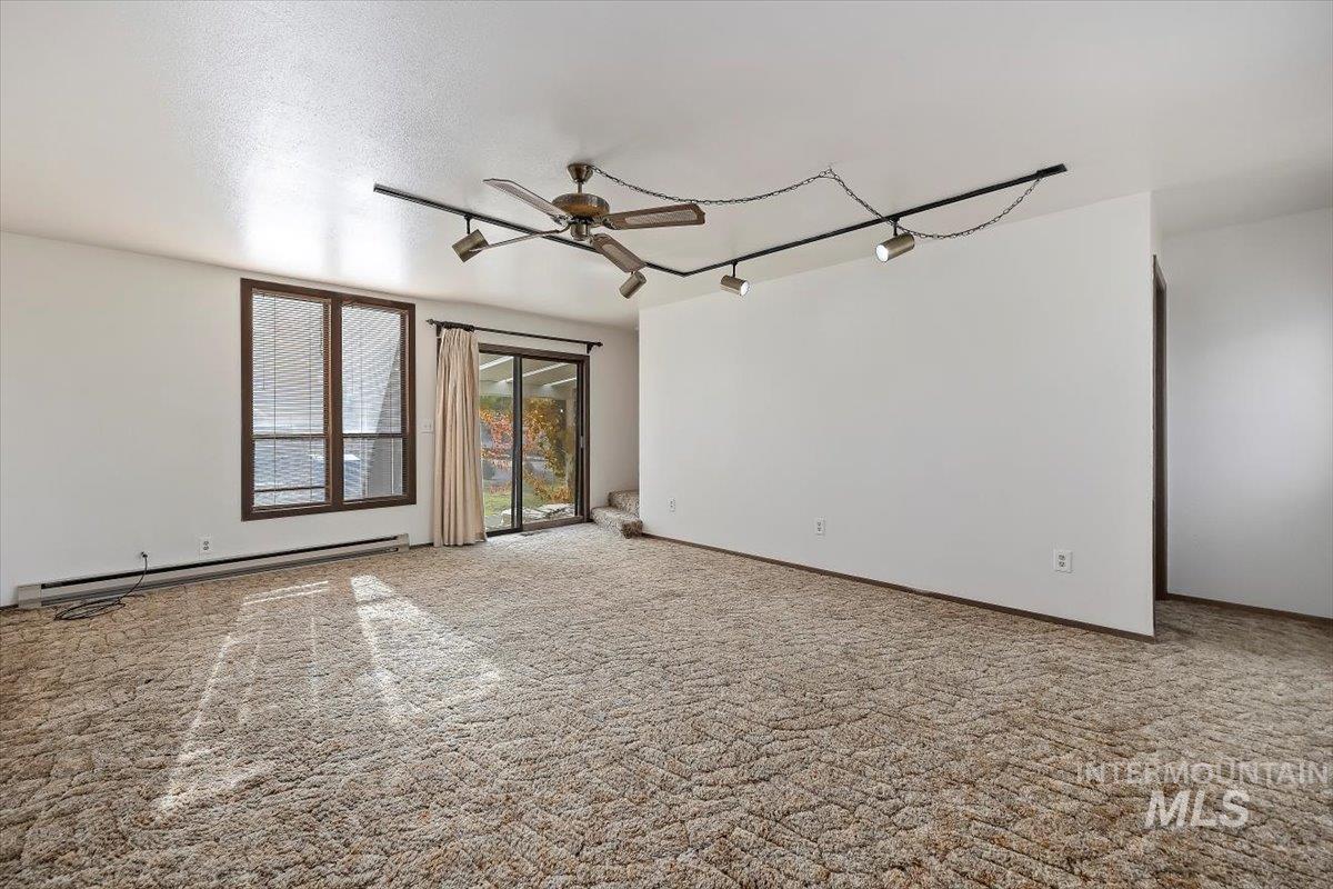 Spare room featuring rail lighting, light carpet, a baseboard heating unit, and a ceiling fan