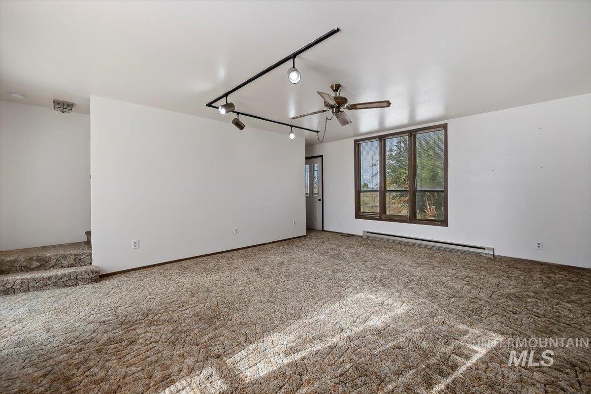 Spare room with rail lighting, carpet flooring, baseboard heating, and a ceiling fan