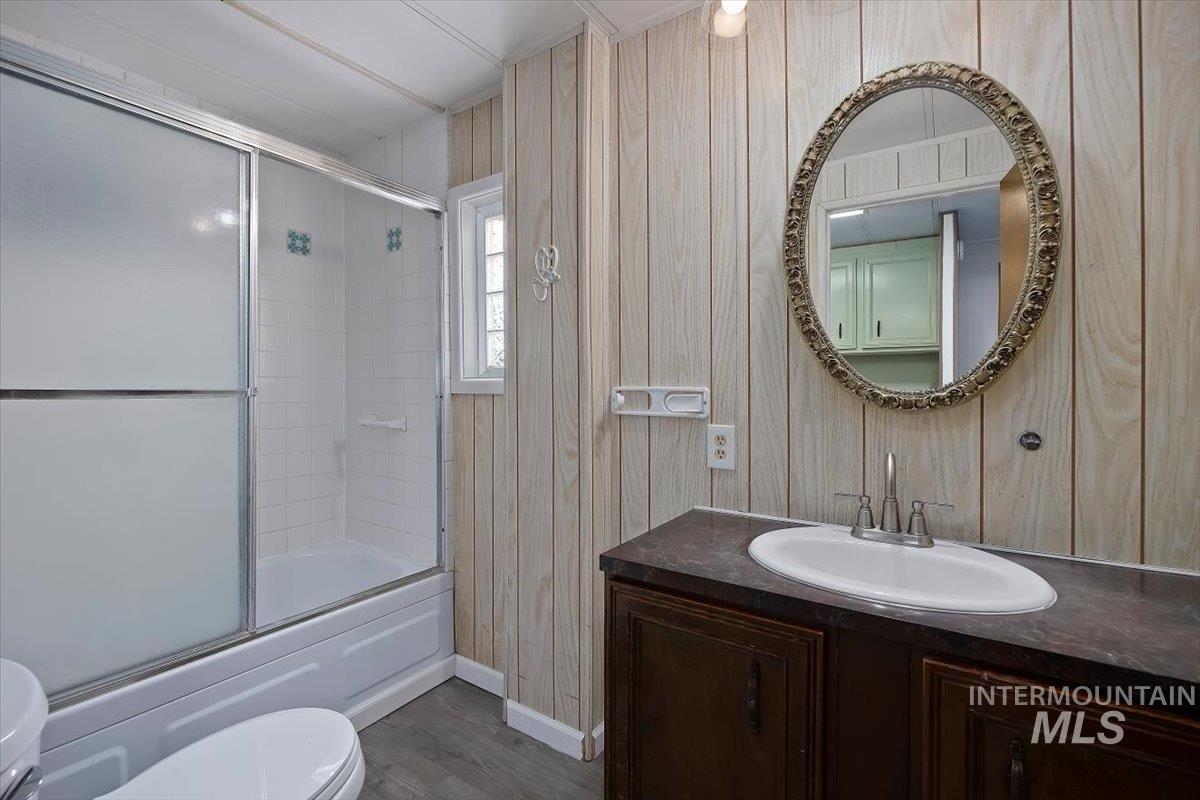 Bathroom featuring vanity, bath / shower combo with glass door, dark wood-style floors, and wooden walls