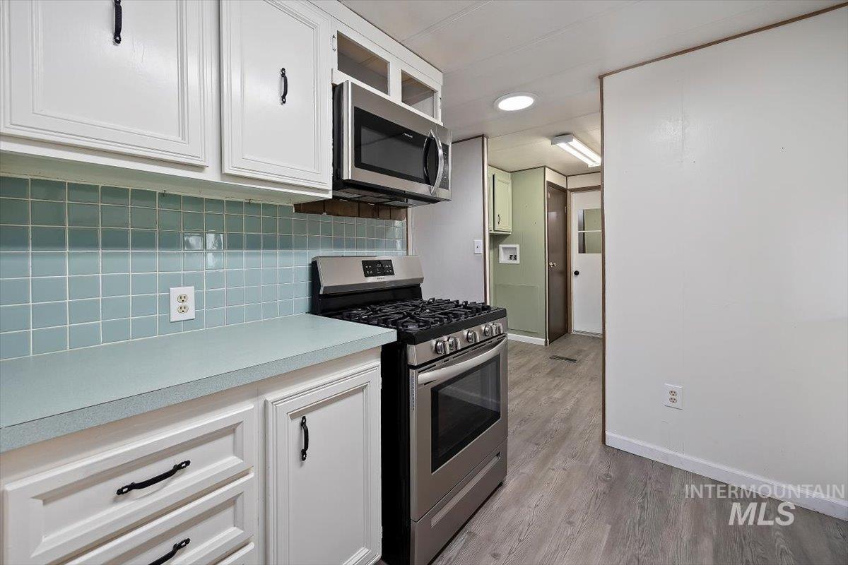Kitchen with appliances with stainless steel finishes, white cabinetry, light countertops, light wood-type flooring, and tasteful backsplash