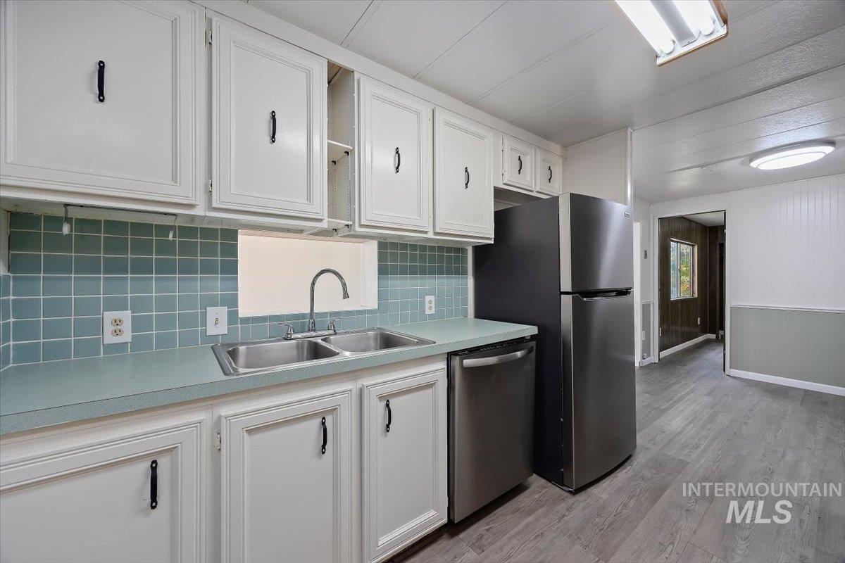 Kitchen featuring white cabinetry, light wood-style floors, light countertops, stainless steel dishwasher, and decorative backsplash
