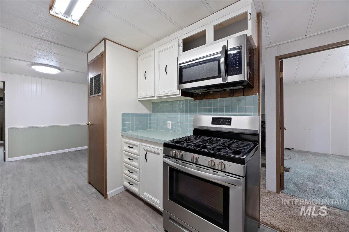 Kitchen featuring white cabinetry, appliances with stainless steel finishes, light countertops, decorative backsplash, and light wood-style floors
