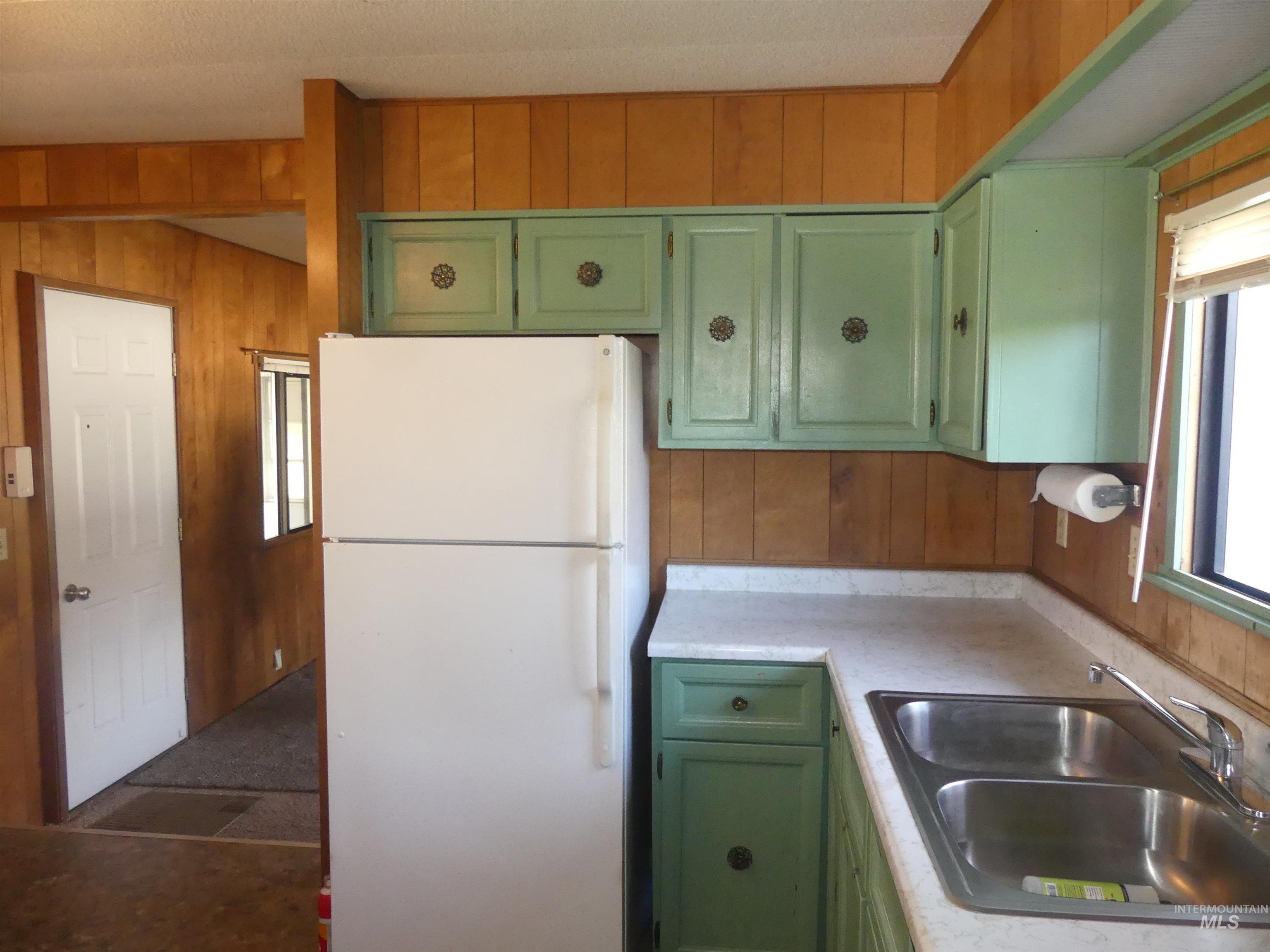 Kitchen featuring green cabinets, wooden walls, freestanding refrigerator, and light countertops