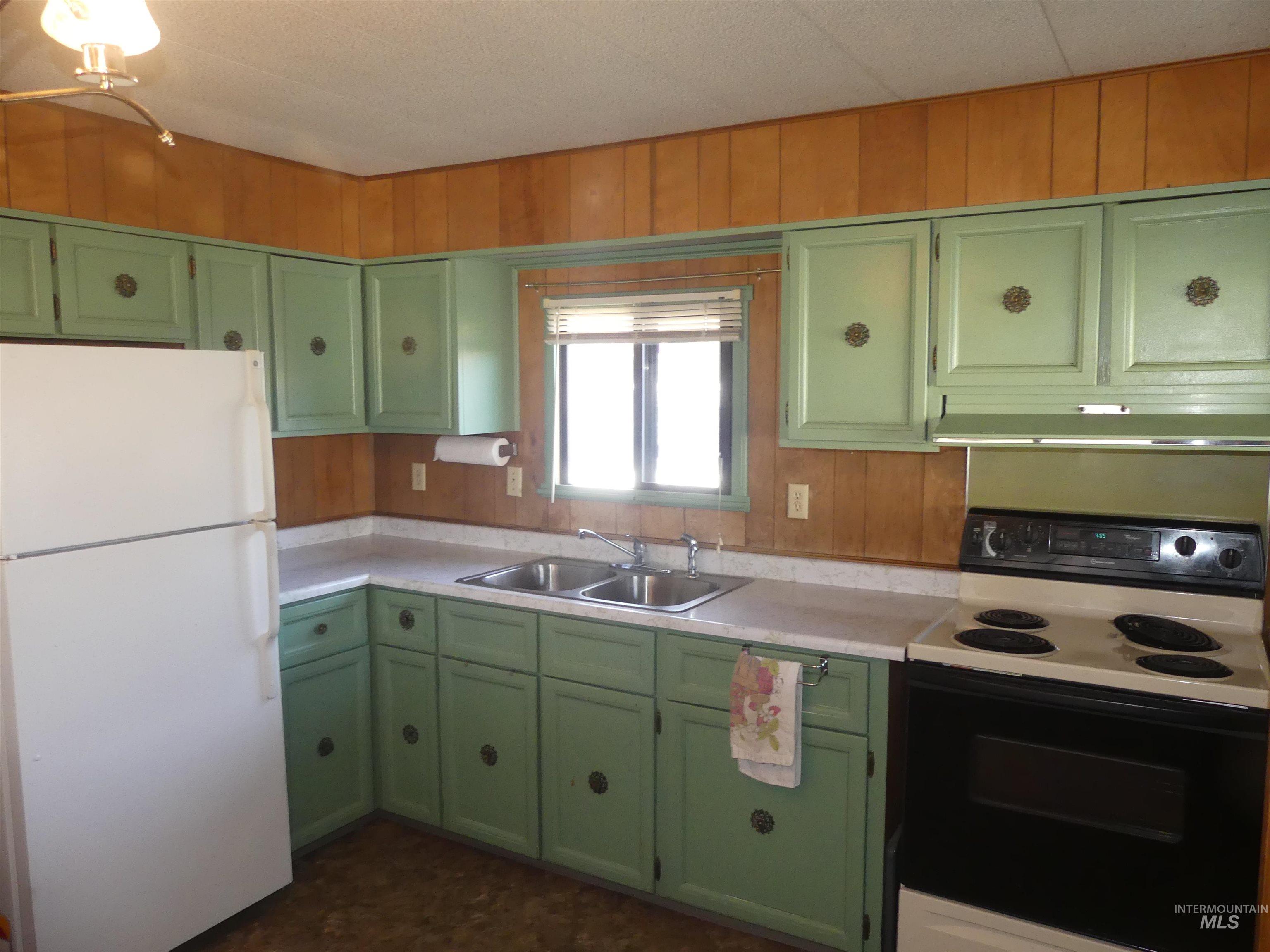 Kitchen featuring green cabinetry, electric stove, freestanding refrigerator, light countertops, and wooden walls