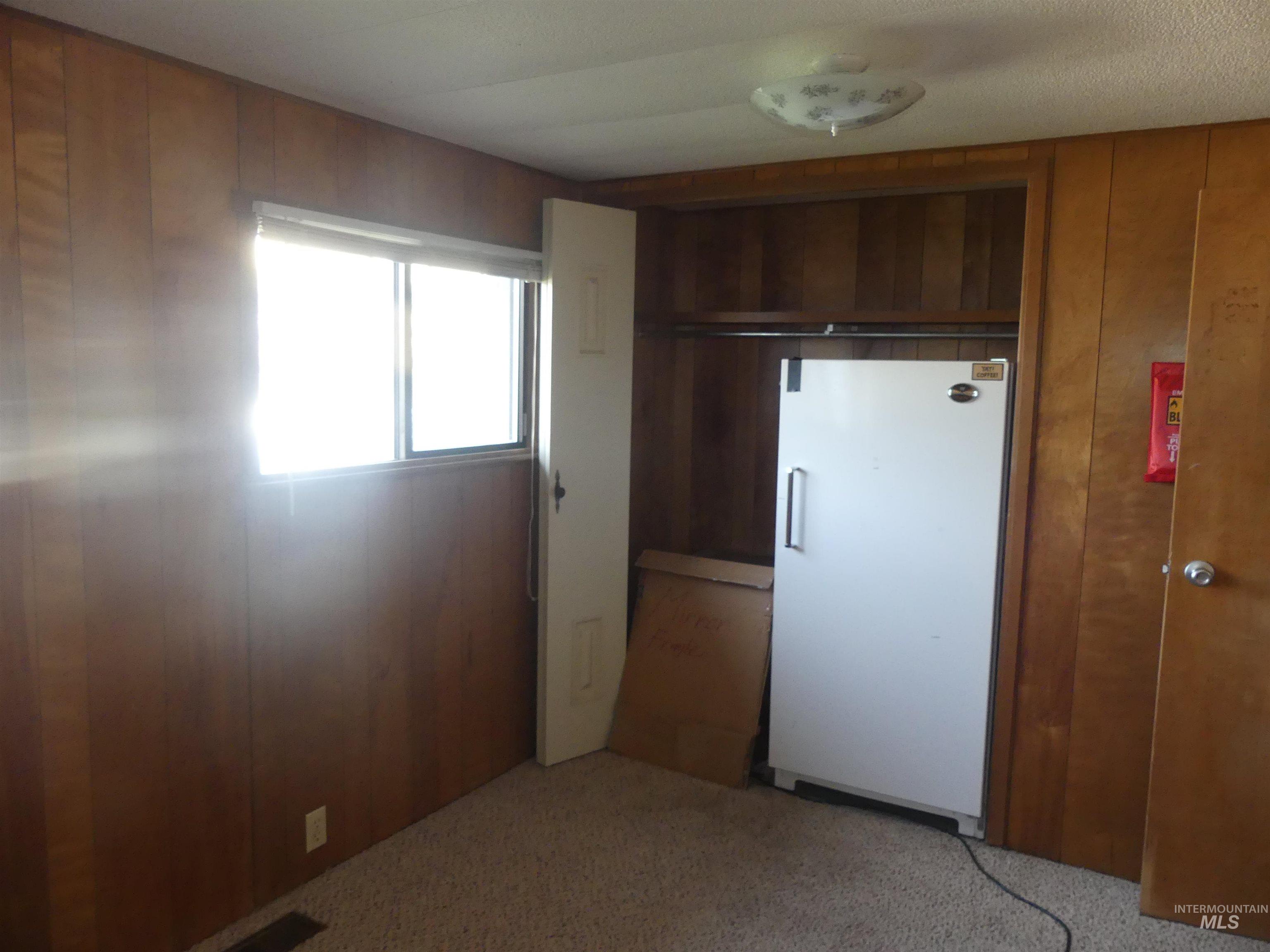 Kitchen with wood walls, freestanding refrigerator, light carpet, and brown cabinetry