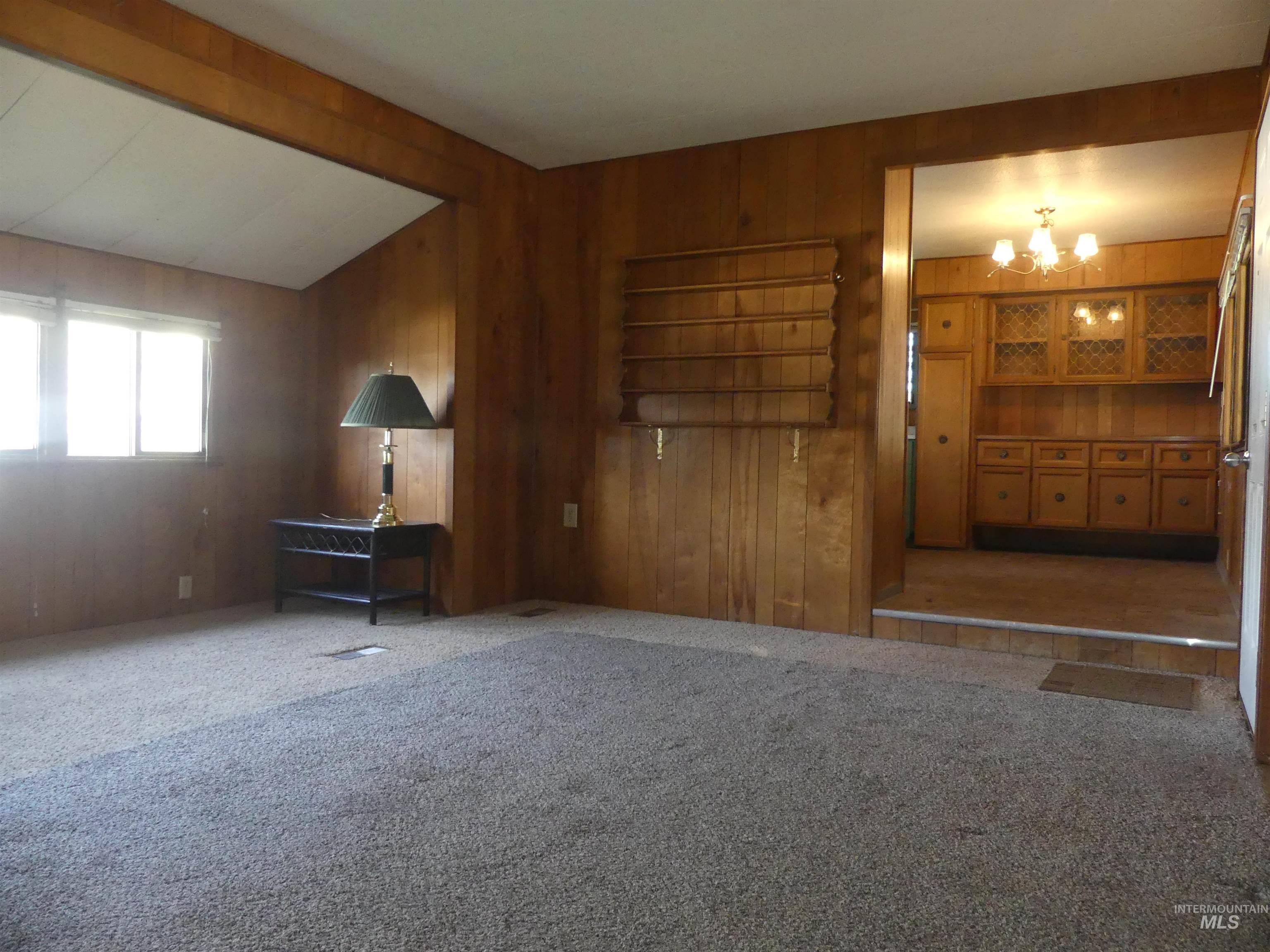Unfurnished living room featuring carpet floors, a chandelier, and wood walls