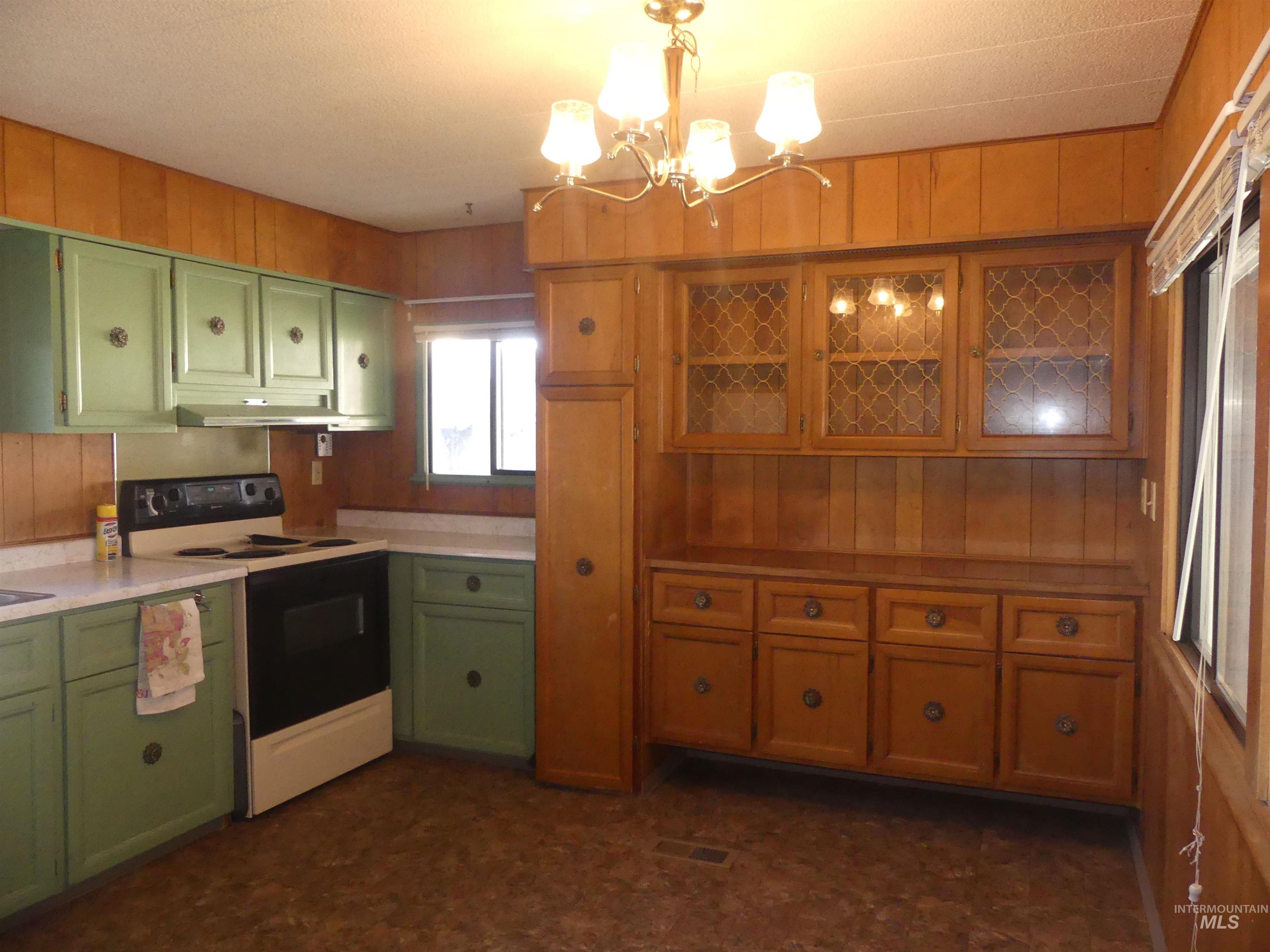 Kitchen featuring green cabinets, wooden walls, electric range, and light countertops