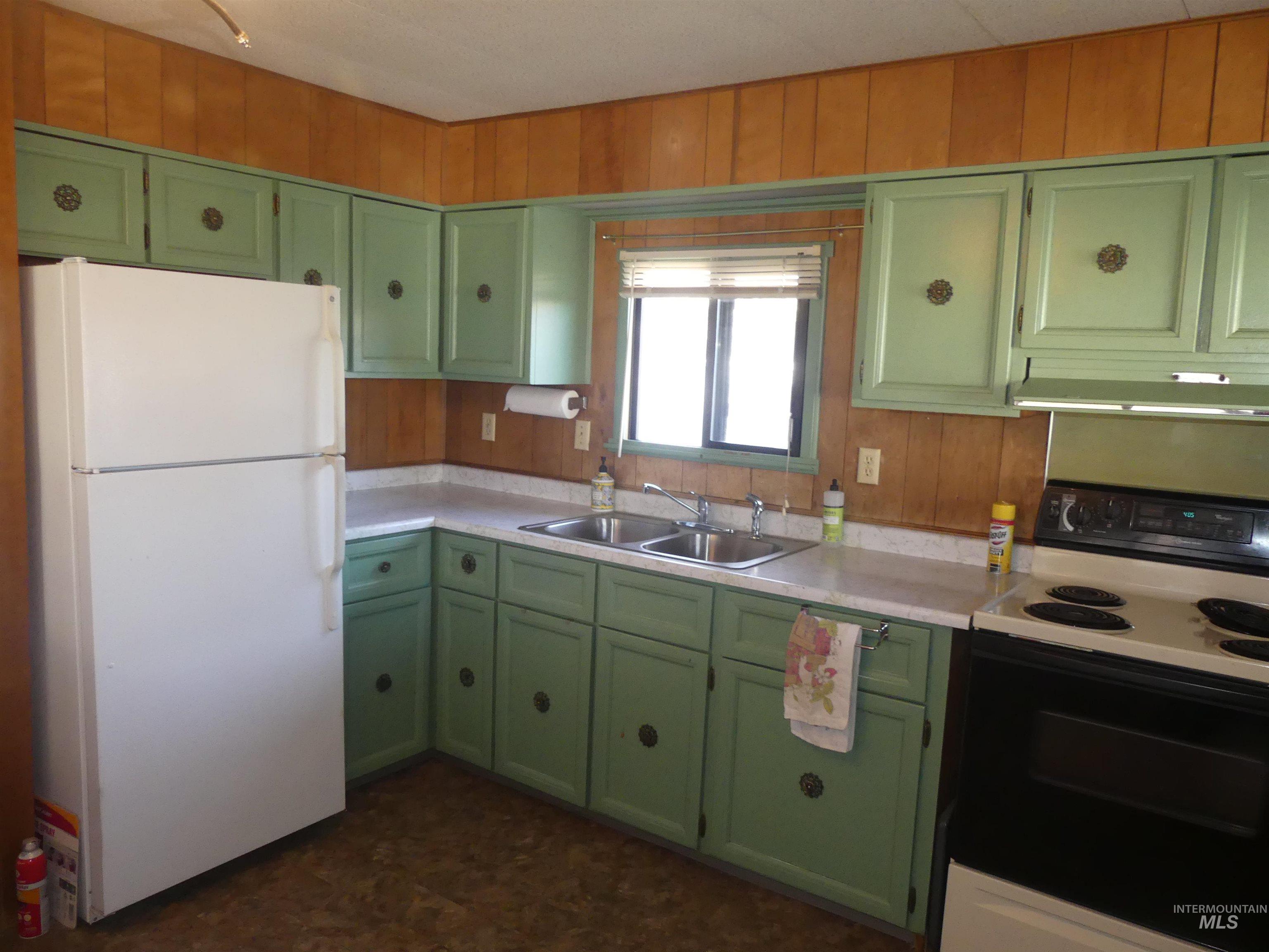 Kitchen featuring green cabinets, electric stove, freestanding refrigerator, light countertops, and wooden walls