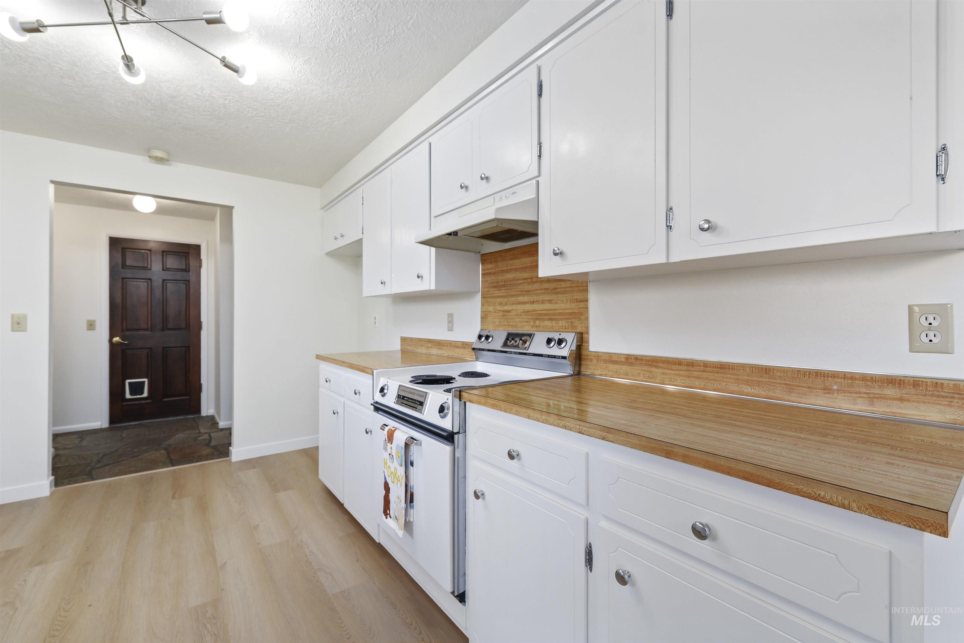 Kitchen with electric range, light wood-style flooring, light countertops, white cabinets, and a textured ceiling