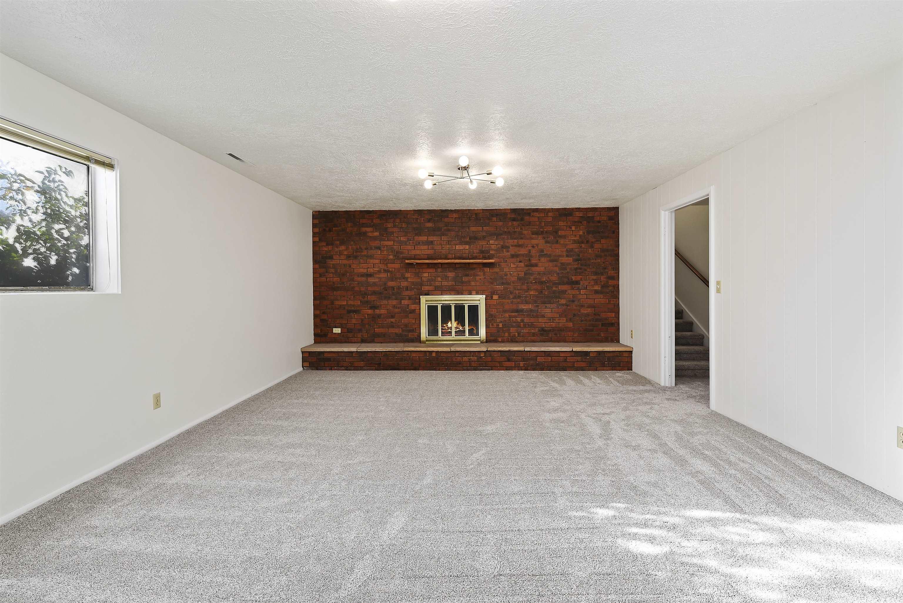 Unfurnished living room with a brick fireplace, carpet flooring, a textured ceiling, and stairway
