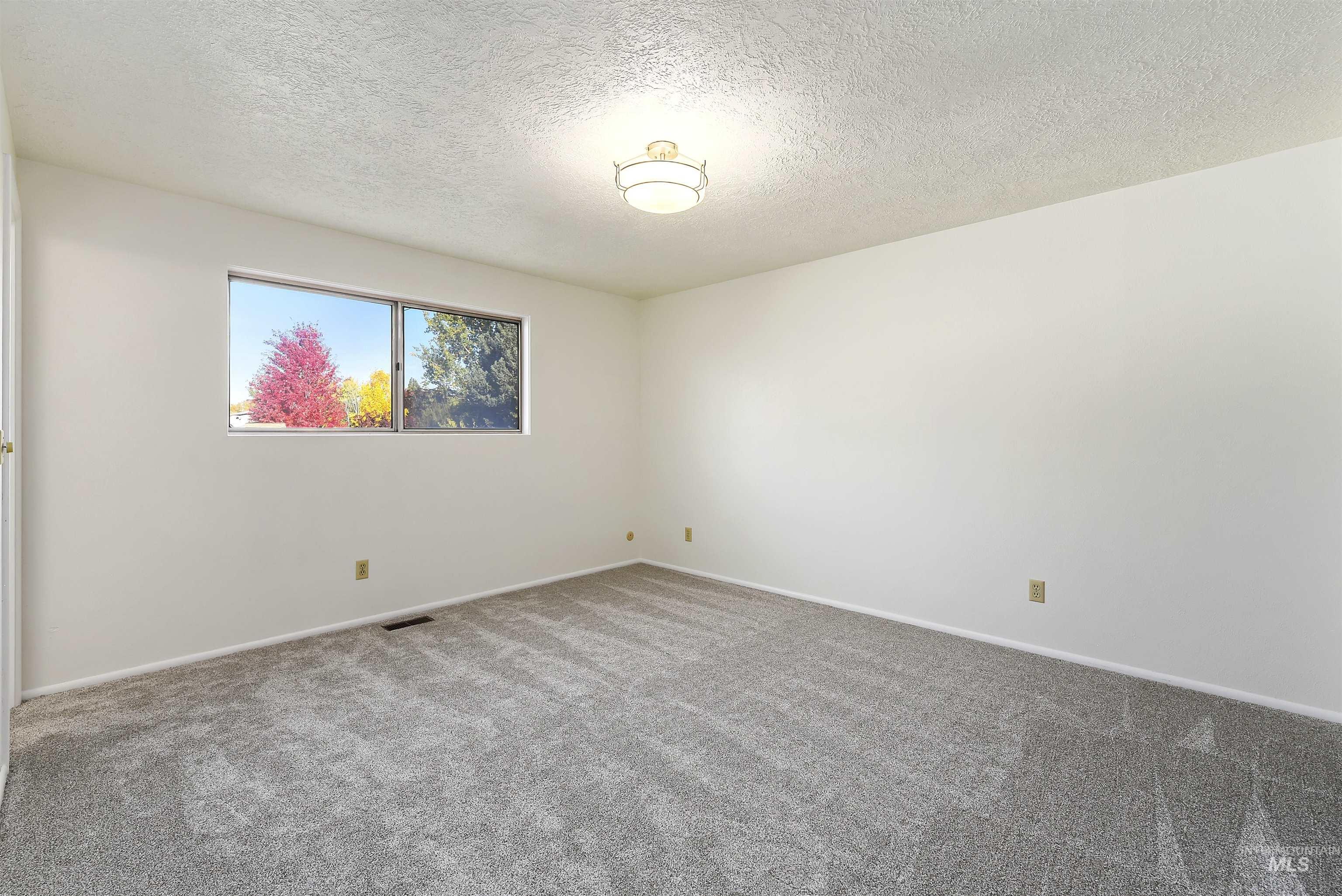 Carpeted empty room featuring a textured ceiling and baseboards