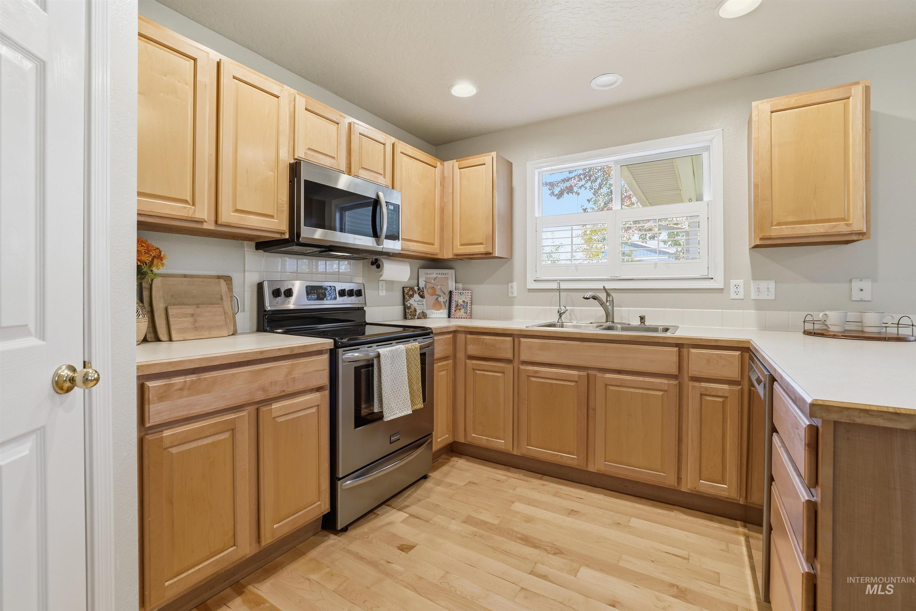 Kitchen with light countertops, stainless steel appliances, light brown cabinets, light wood finished floors, and recessed lighting