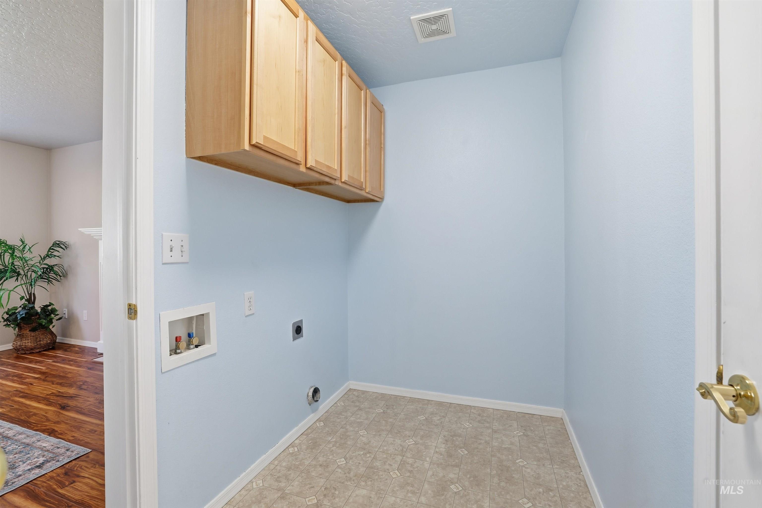 Laundry room featuring hookup for an electric dryer, cabinet space, a textured ceiling, and hookup for a washing machine