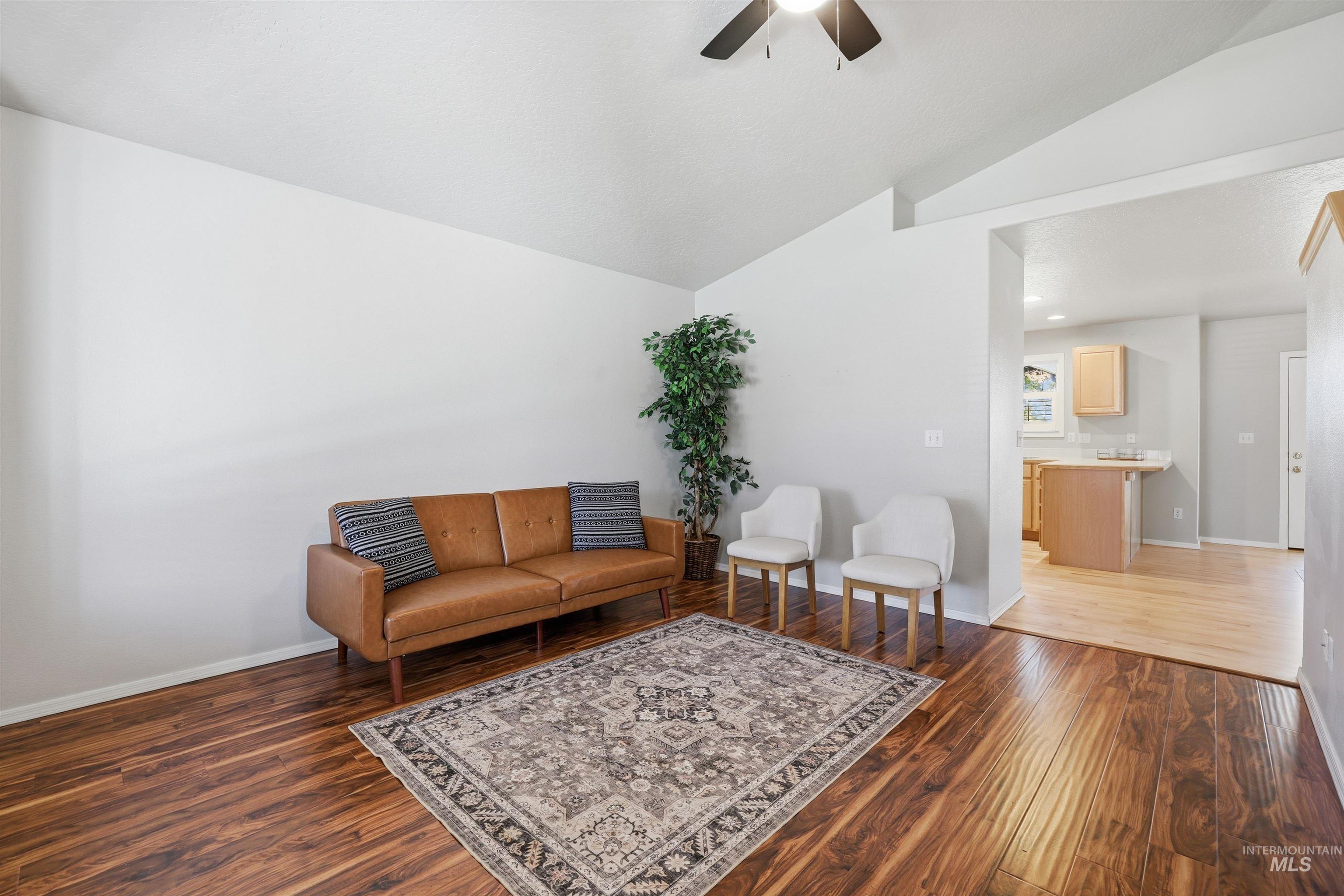Living area featuring vaulted ceiling, dark wood-style flooring, and a ceiling fan
