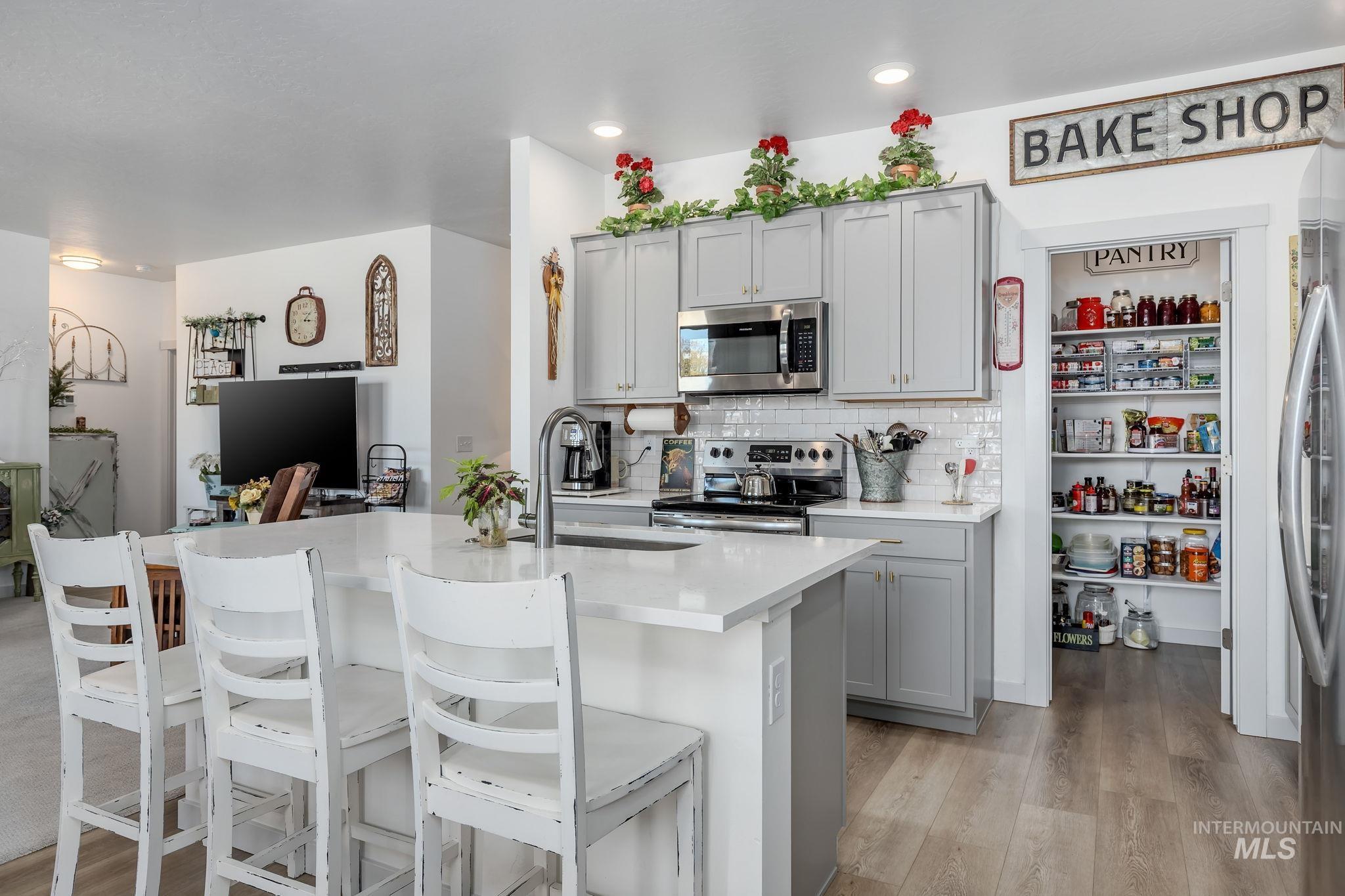 Kitchen with gray cabinetry, stainless steel appliances, tasteful backsplash, and light wood finished floors