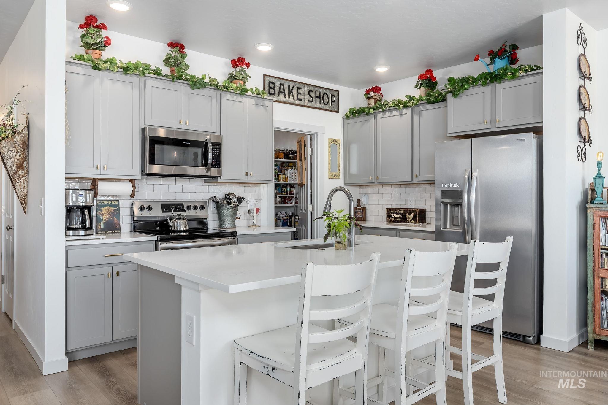 Kitchen with appliances with stainless steel finishes, a kitchen breakfast bar, a kitchen island with sink, gray cabinetry, and light wood-type flooring