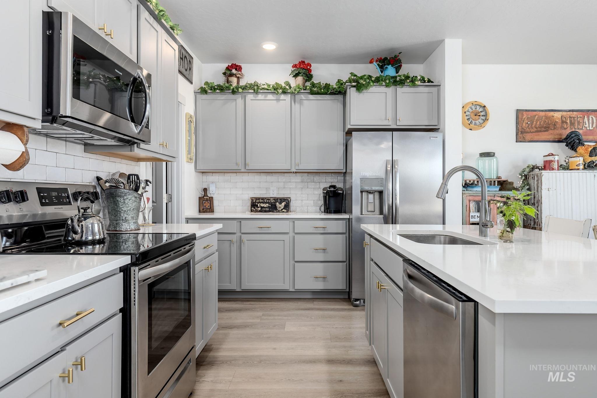 Kitchen featuring appliances with stainless steel finishes, gray cabinets, decorative backsplash, and light wood-style floors