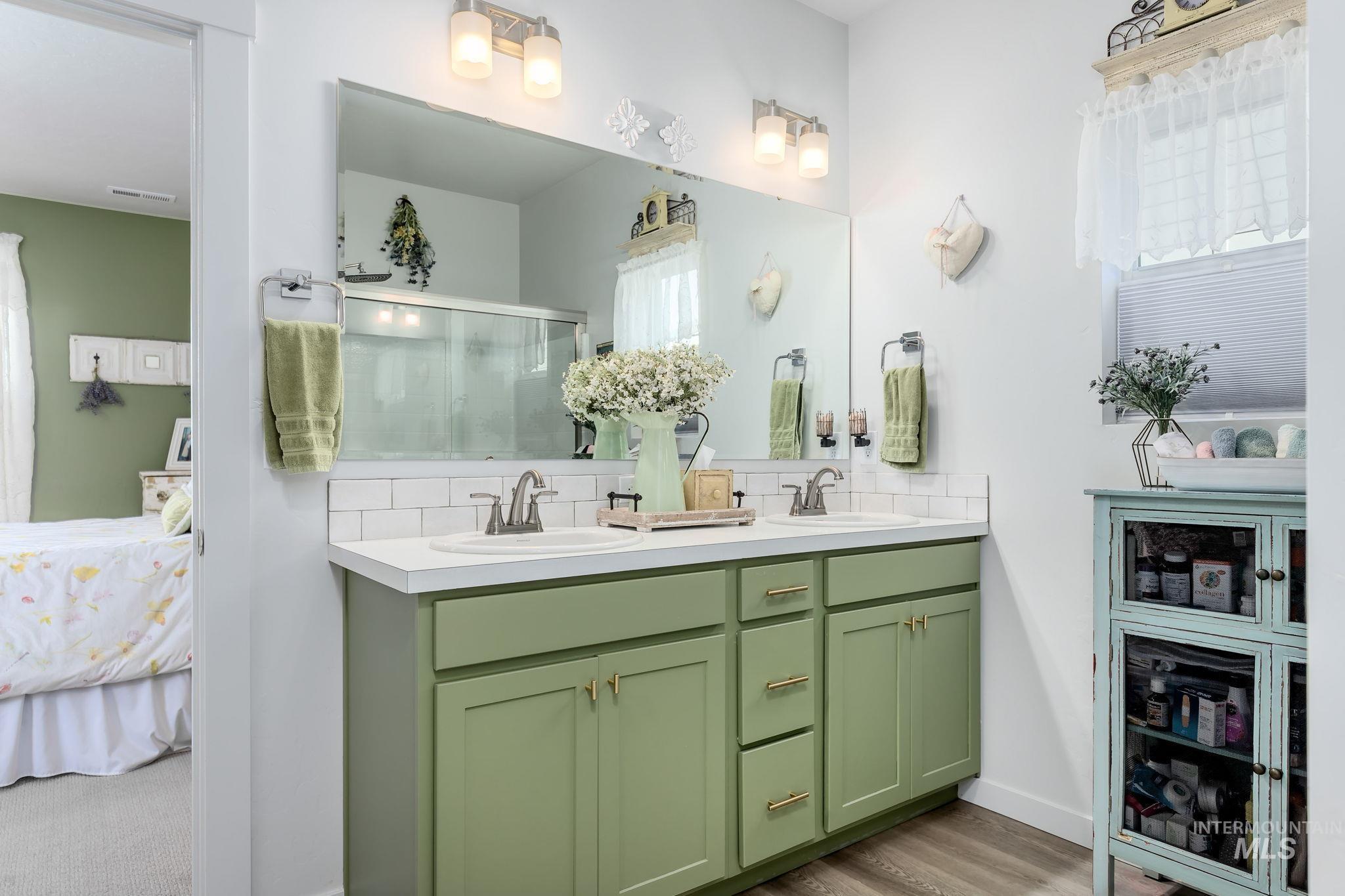Ensuite bathroom featuring double vanity, a stall shower, decorative backsplash, and light wood finished floors