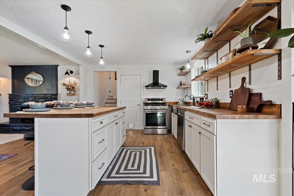 Kitchen with wooden counters, open shelves, stainless steel appliances, a kitchen bar, and wall chimney range hood