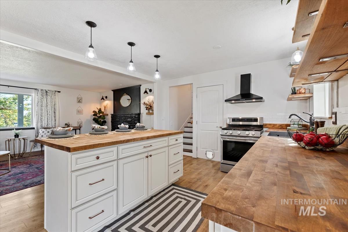 Kitchen featuring wood counters, decorative light fixtures, stainless steel gas stove, wall chimney range hood, and light wood-style flooring