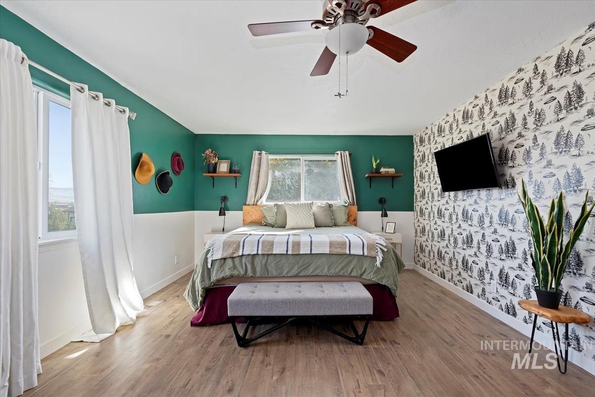 Bedroom featuring an accent wall, wallpapered walls, wood finished floors, and a ceiling fan