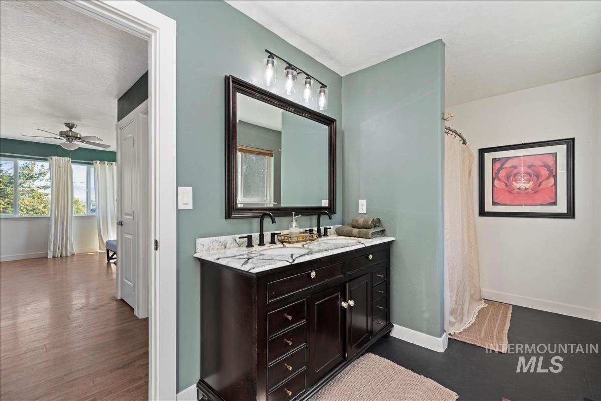 Full bath with double vanity, a shower with curtain, a ceiling fan, and wood finished floors
