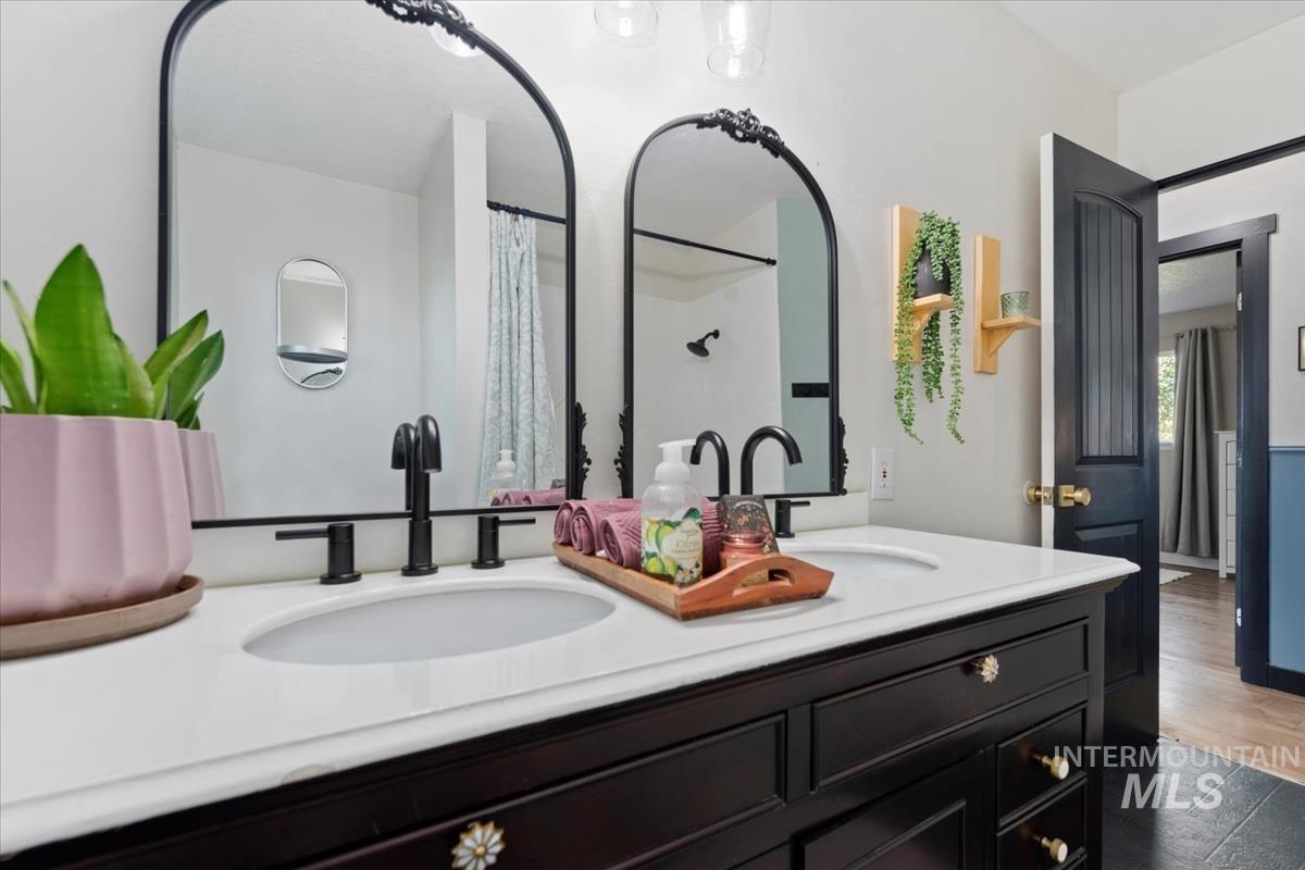 Full bath with double vanity, a shower with curtain, and dark wood-style floors