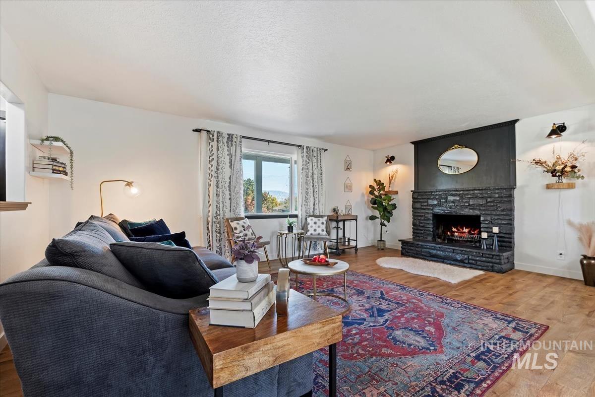 Living room featuring wood finished floors, a stone fireplace, and a textured ceiling