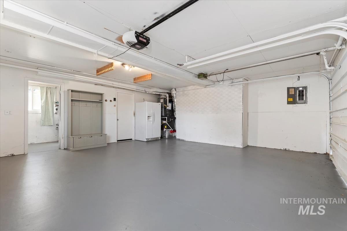 Garage with white fridge with ice dispenser, electric panel, and a garage door opener