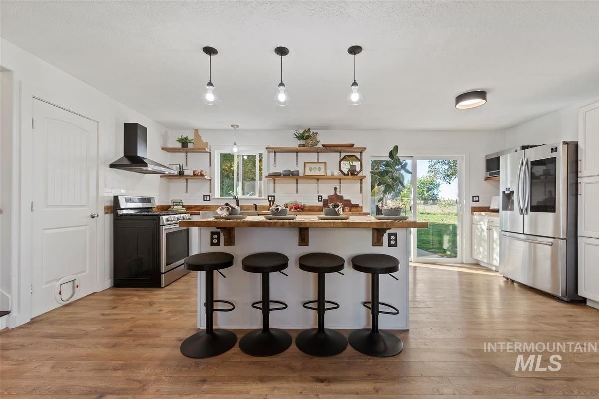 Kitchen with a breakfast bar, stainless steel appliances, light wood-style floors, open shelves, and hanging light fixtures