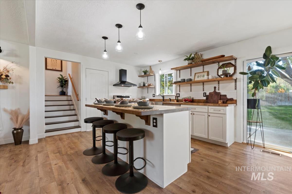 Kitchen featuring open shelves, a kitchen breakfast bar, white cabinets, pendant lighting, and light wood-style floors