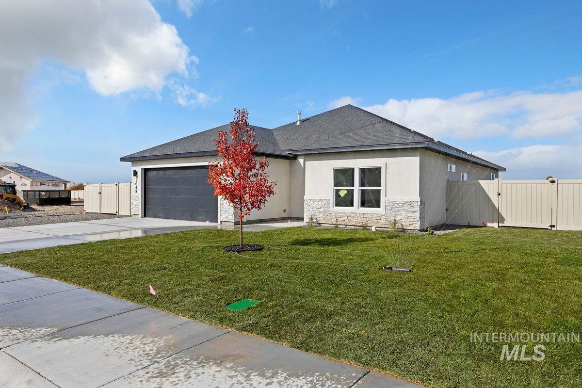 Ranch-style home with a gate, stucco siding, stone siding, and roof with shingles