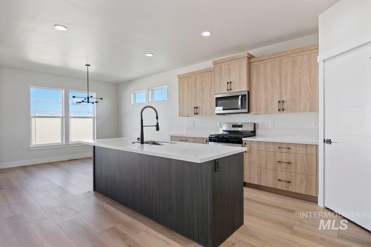 Kitchen with light brown cabinets, decorative light fixtures, an island with sink, appliances with stainless steel finishes, and recessed lighting