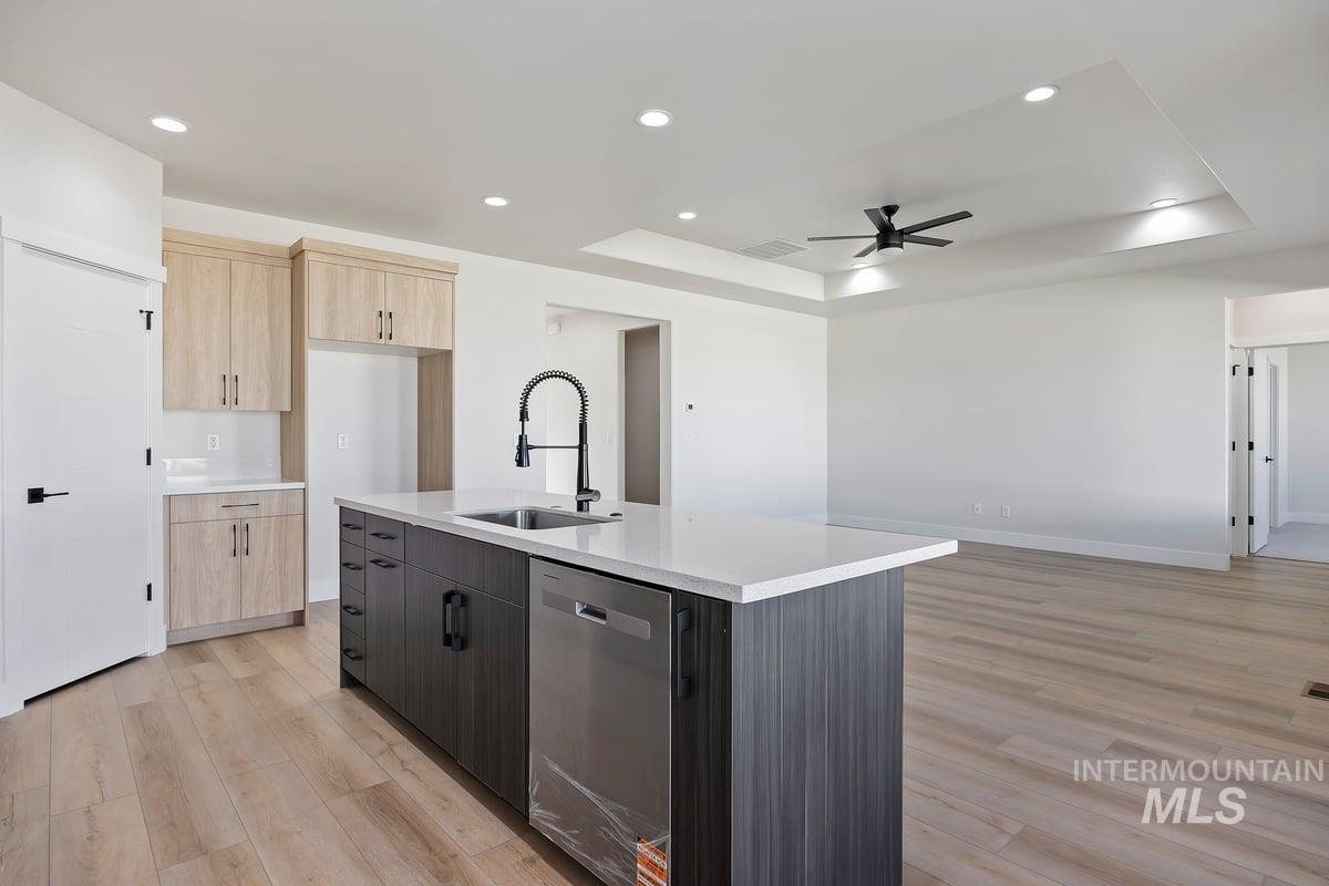 Kitchen featuring light brown cabinets, a tray ceiling, recessed lighting, dishwasher, and light wood finished floors