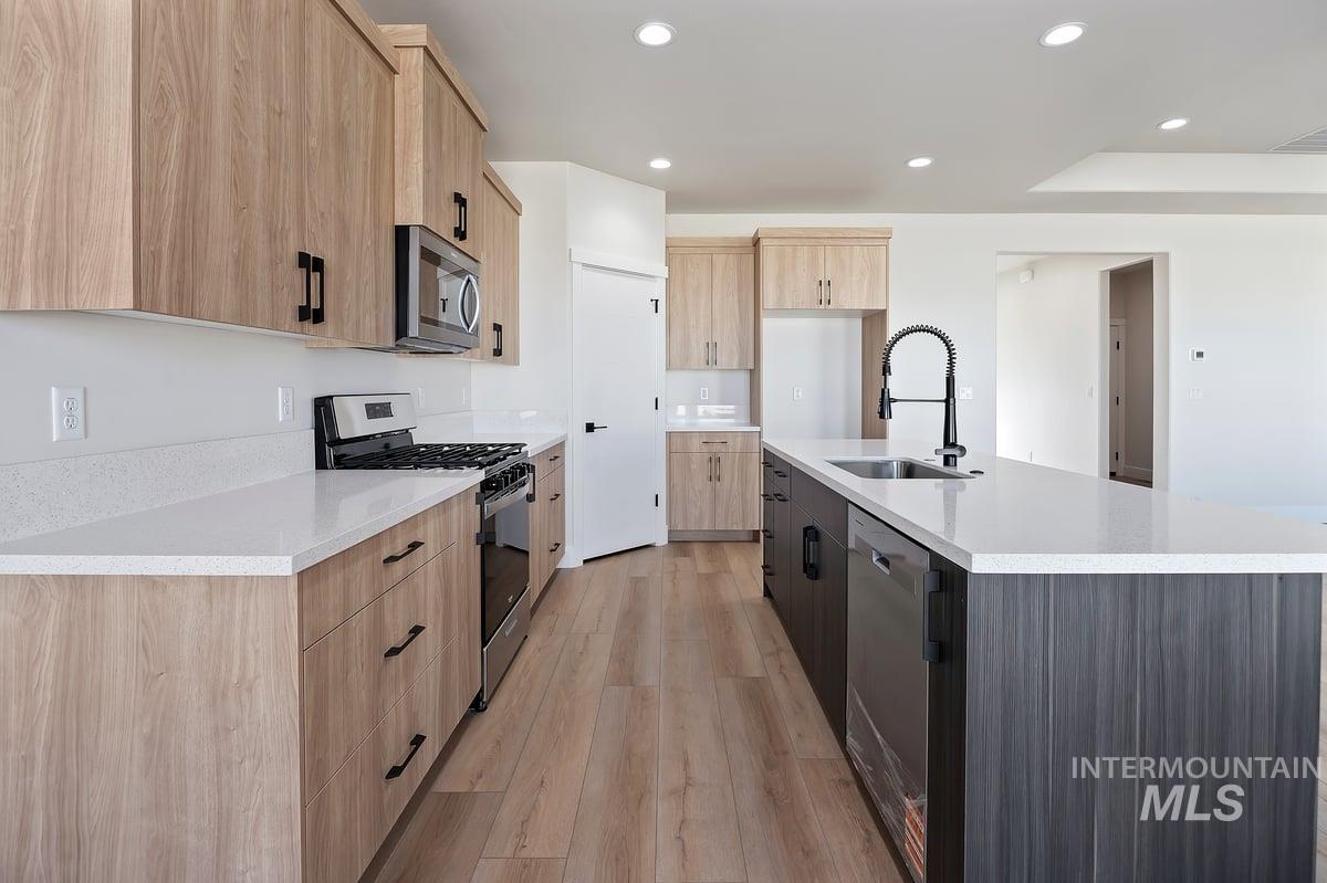 Kitchen featuring light brown cabinetry, stainless steel appliances, recessed lighting, light stone counters, and light wood finished floors
