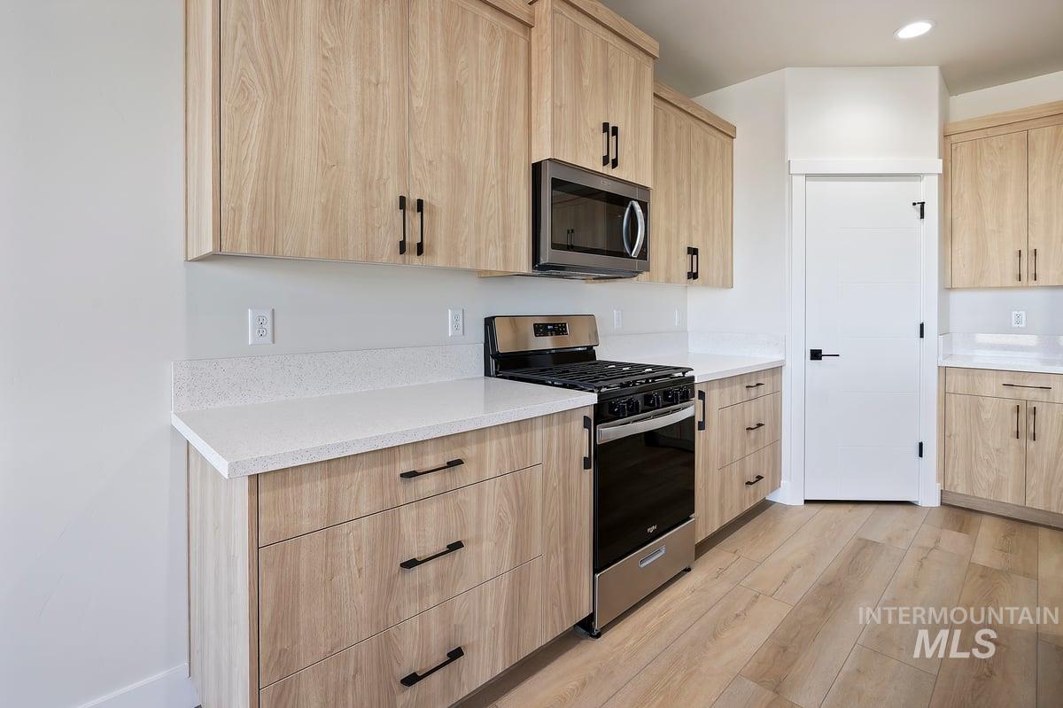 Kitchen with light brown cabinets, stainless steel appliances, light wood-style flooring, light stone counters, and recessed lighting