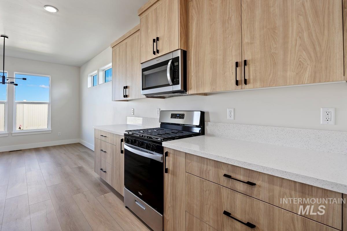 Kitchen featuring light brown cabinetry, appliances with stainless steel finishes, light stone countertops, light wood-style floors, and pendant lighting
