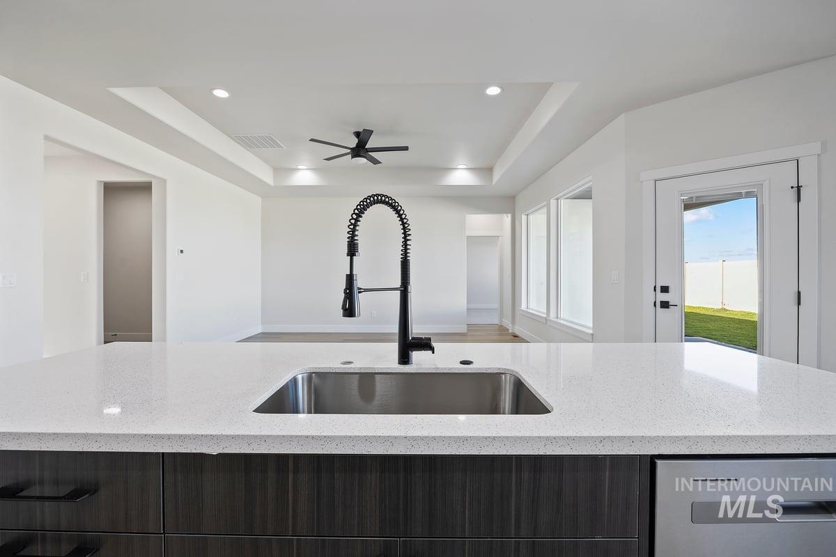 Kitchen featuring a raised ceiling, modern cabinets, stainless steel dishwasher, light stone countertops, and recessed lighting