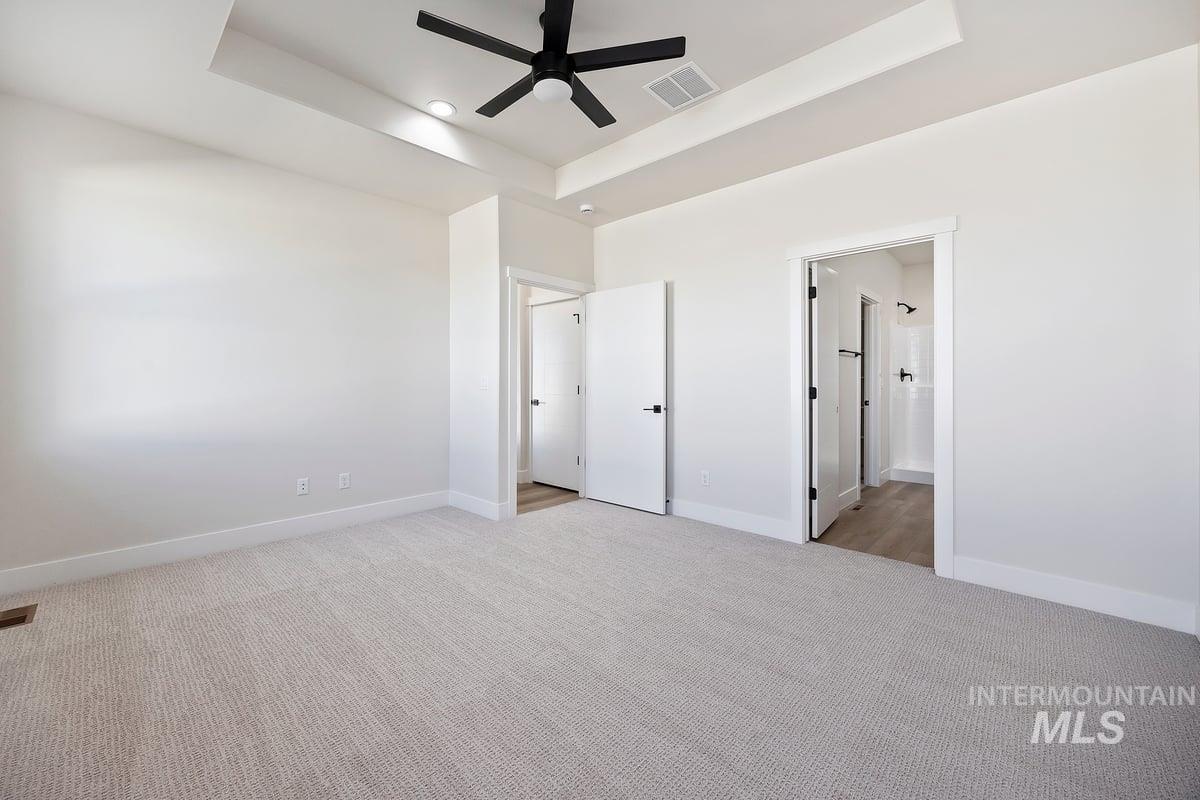 Unfurnished bedroom with a raised ceiling, light carpet, a ceiling fan, and ensuite bathroom