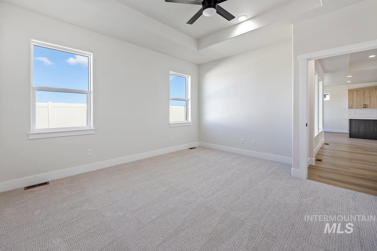 Unfurnished room featuring a raised ceiling, light colored carpet, ceiling fan, and recessed lighting